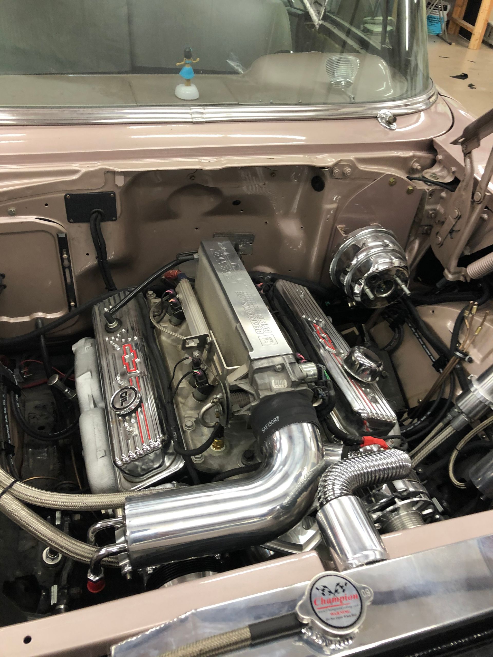 A high-angle view of a customized, light pink vintage car engine bay featuring a polished silver engine and radiator.