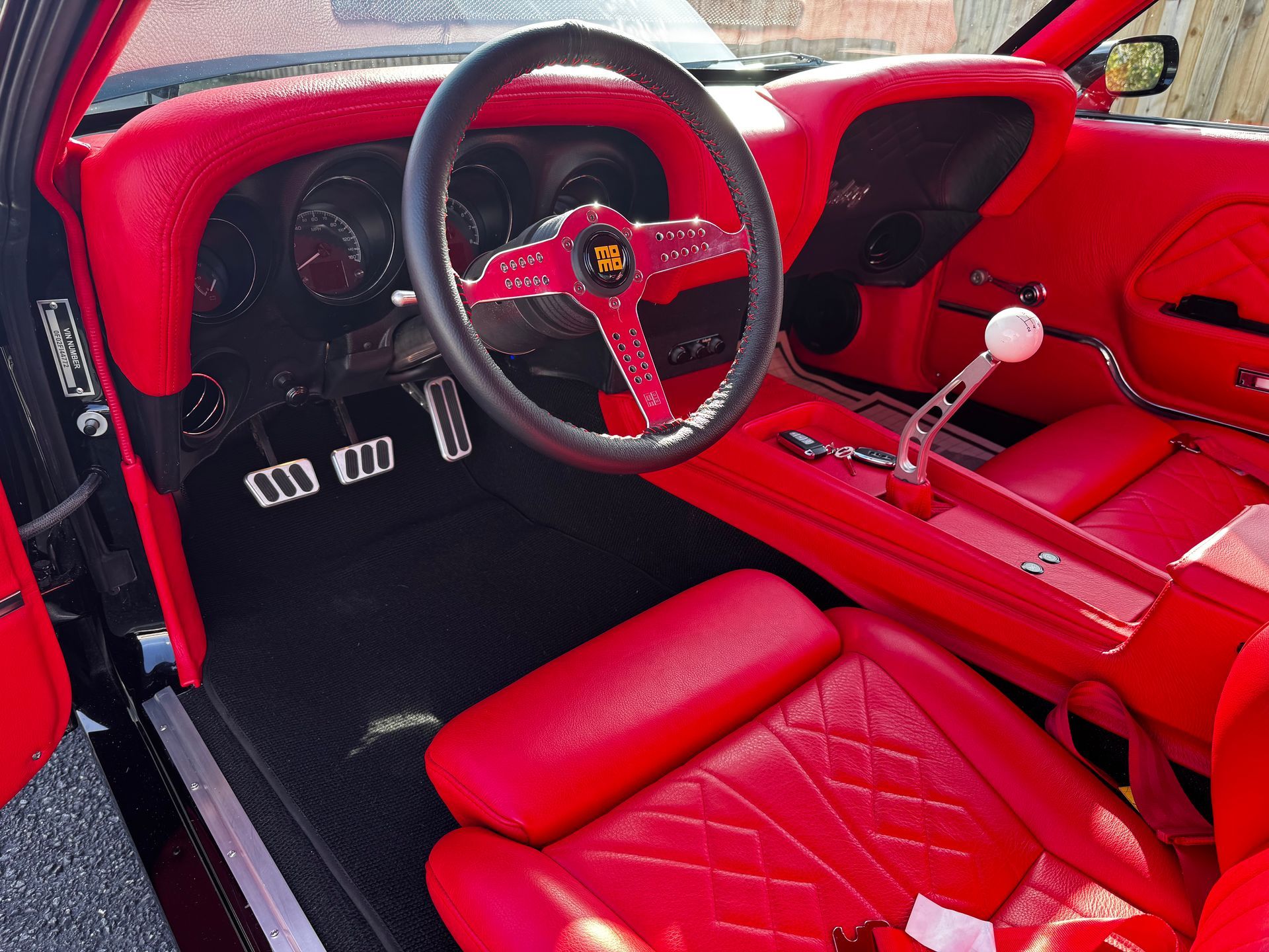The vibrant red interior of a classic car, featuring matching leather seats, a custom steering wheel, and gear shifter.