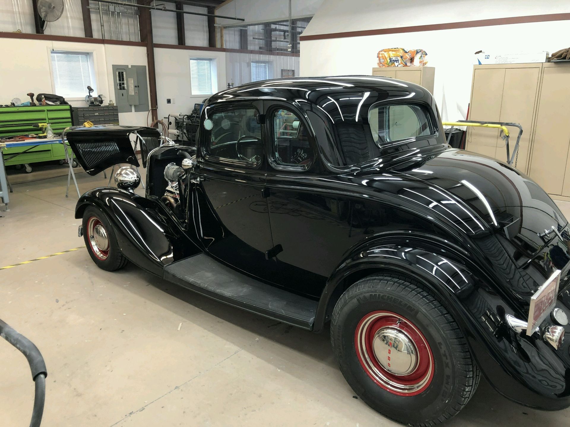 A shiny black vintage coupe parked in a bright auto repair shop.