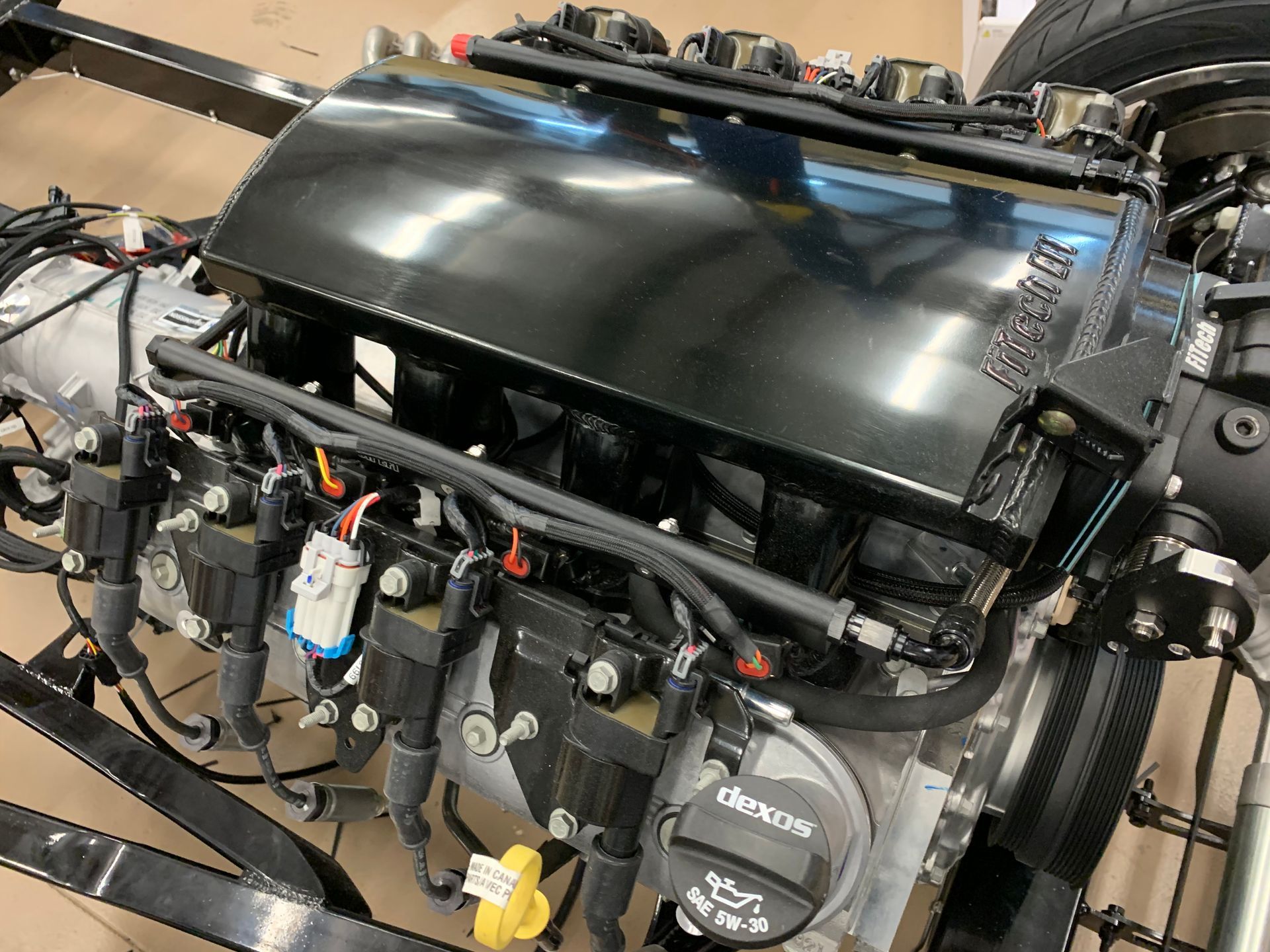 A high-angle view of a clean black car engine with various electrical components, wires, and oil cap visible.