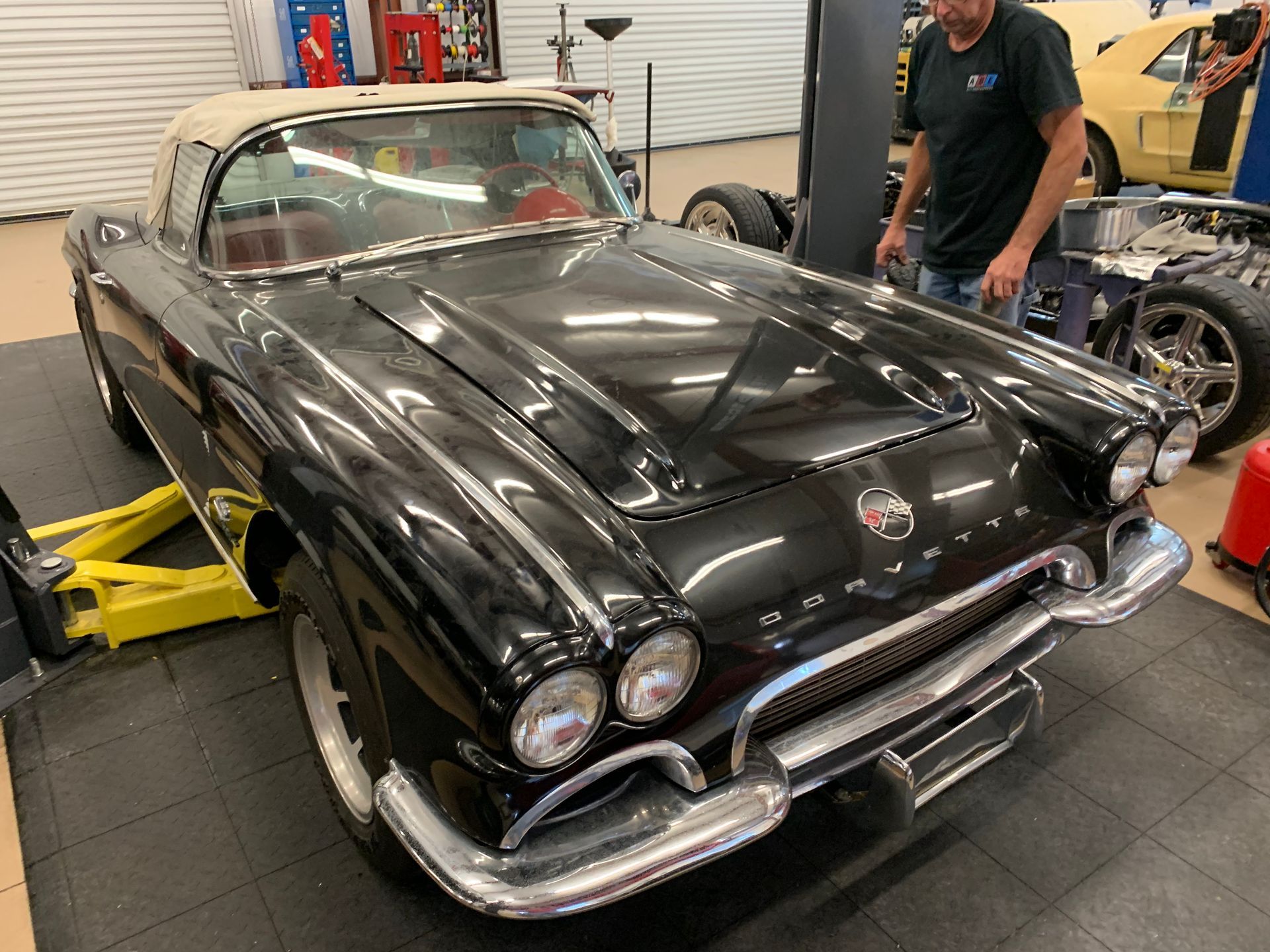 A black 1961 Chevrolet Corvette convertible parked in a professional auto garage.