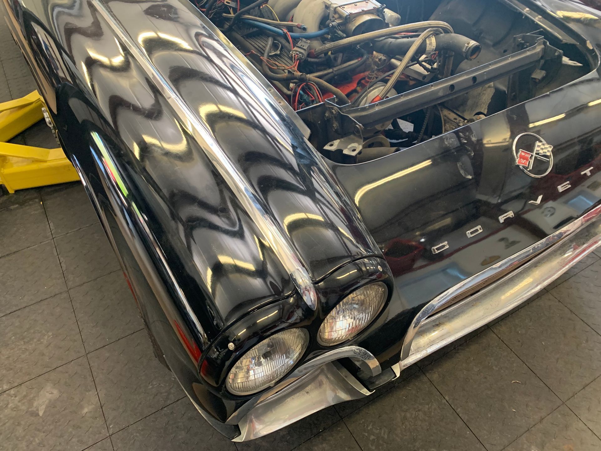 Front view of a black vintage Corvette with chrome trim and dual headlights, parked on a shop floor.