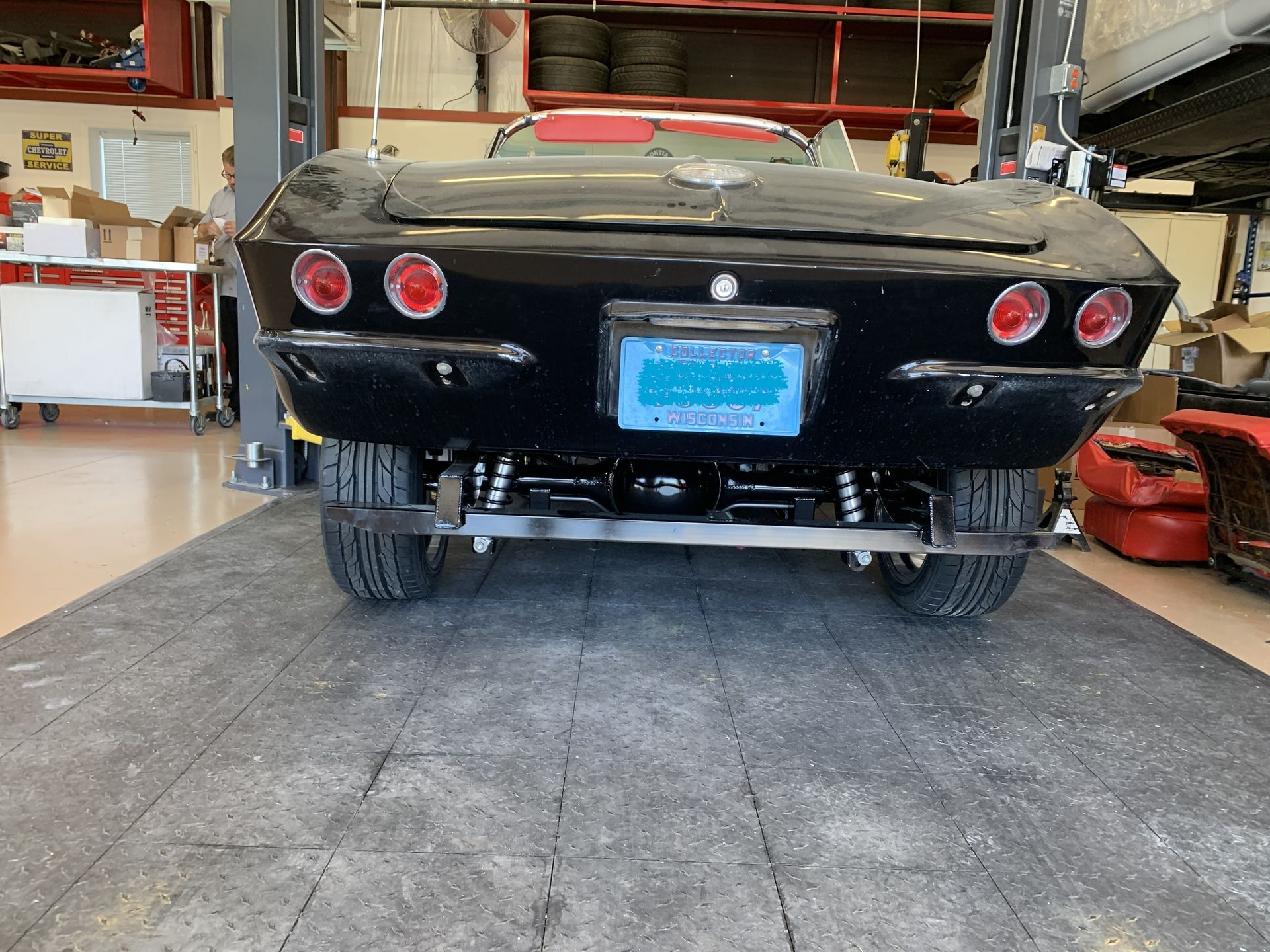 Rear view of a black classic Corvette raised on a car lift inside an automotive repair shop.