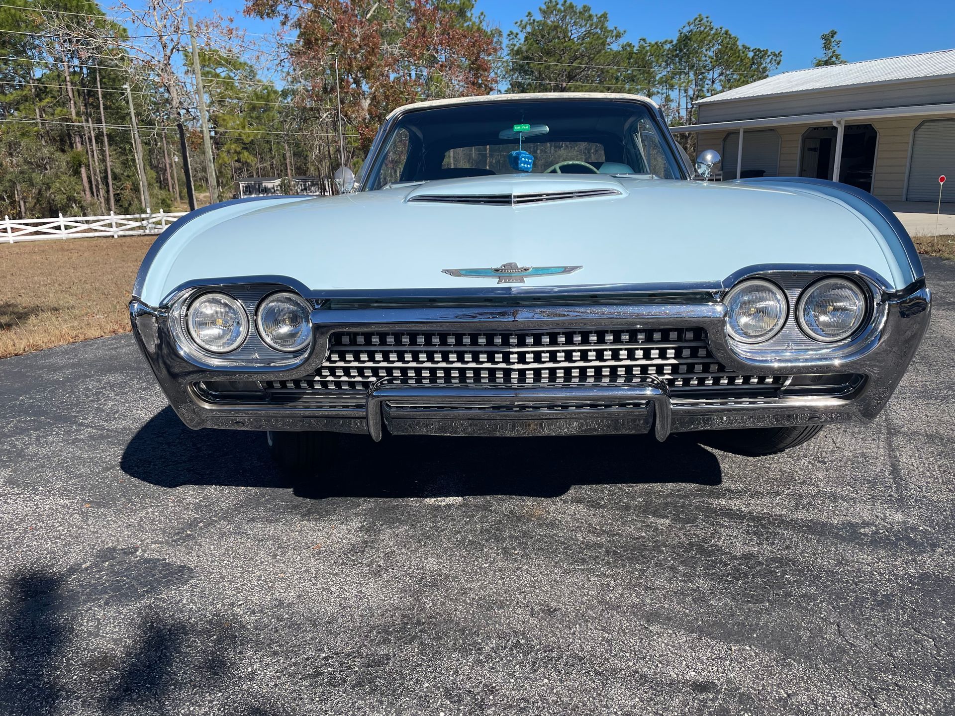 A light blue vintage Ford Thunderbird parked on an asphalt driveway under a clear sky.