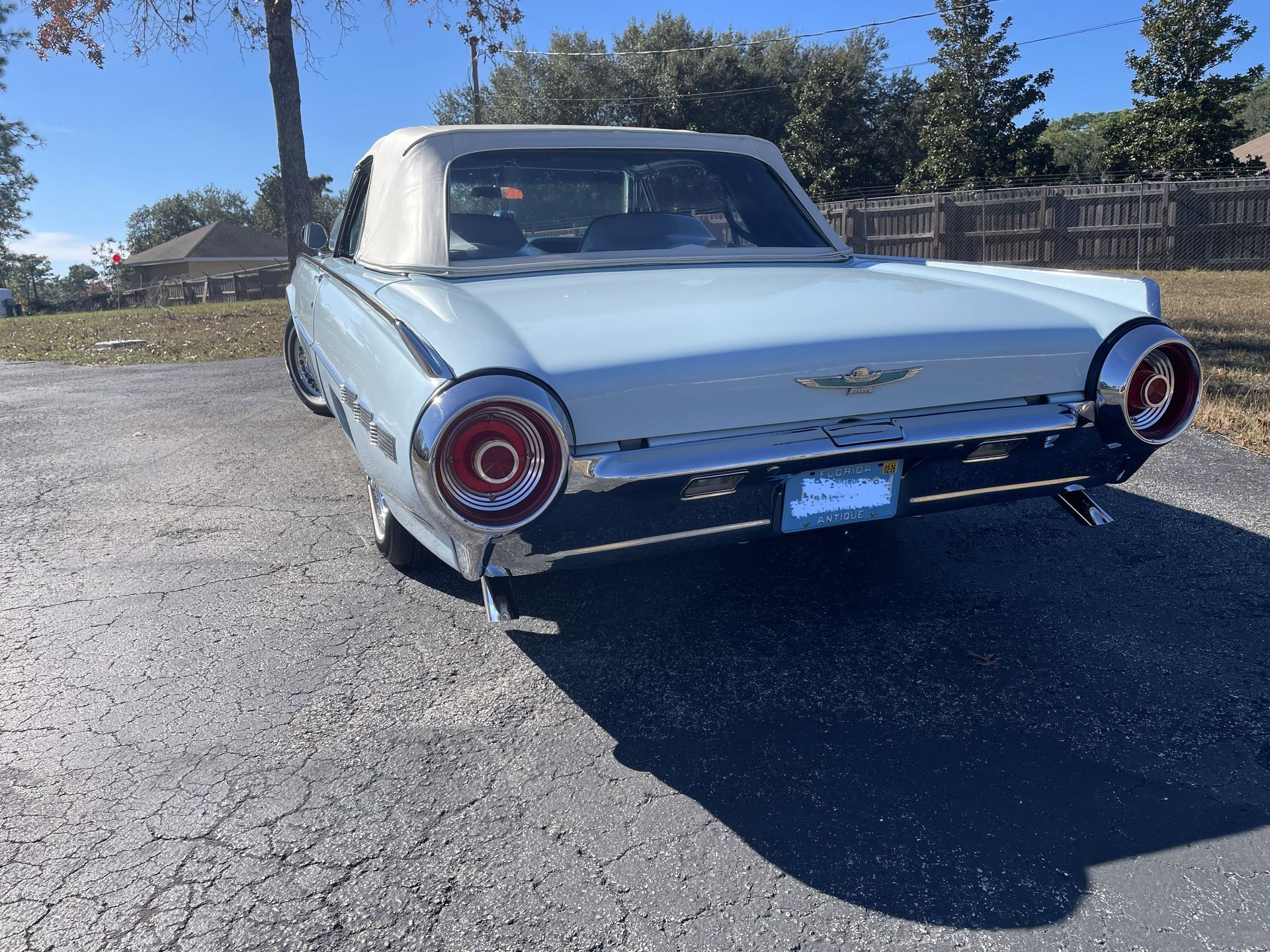 A light blue vintage Ford Thunderbird convertible parked outdoors on an asphalt surface under a clear blue sky.