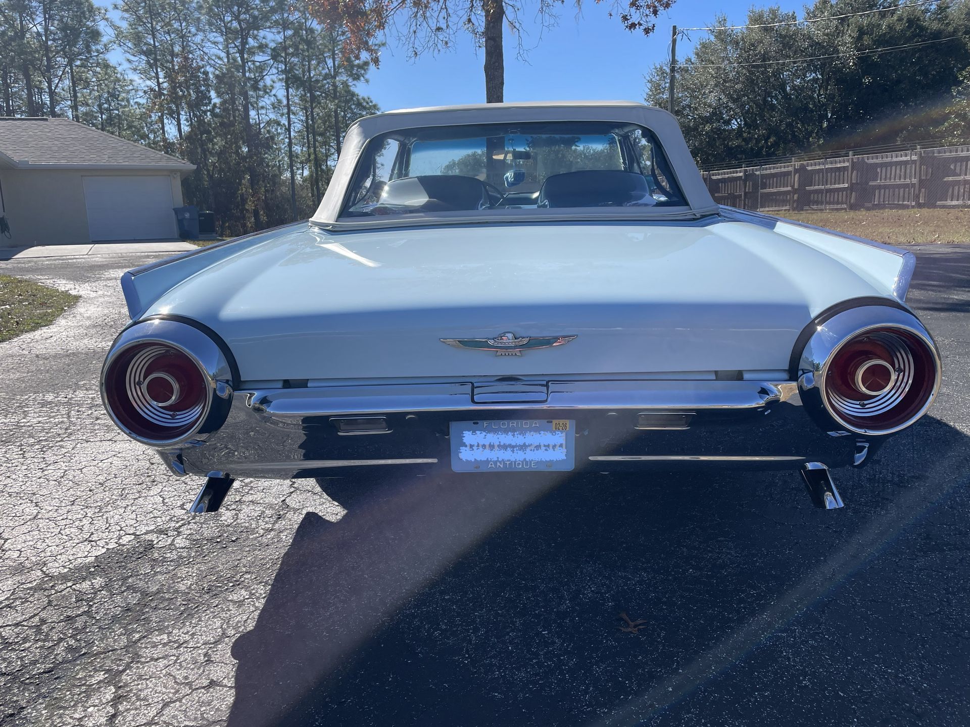 Rear view of a light blue classic Ford Thunderbird convertible parked on an asphalt driveway under a clear sky.
