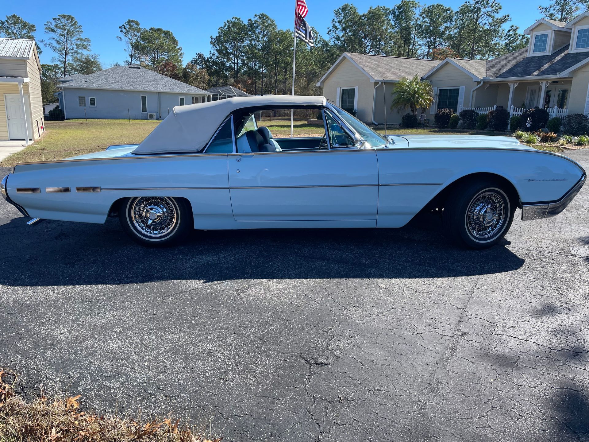 Side profile of a vintage, light blue Ford Thunderbird convertible with a tan top parked on a paved lot.