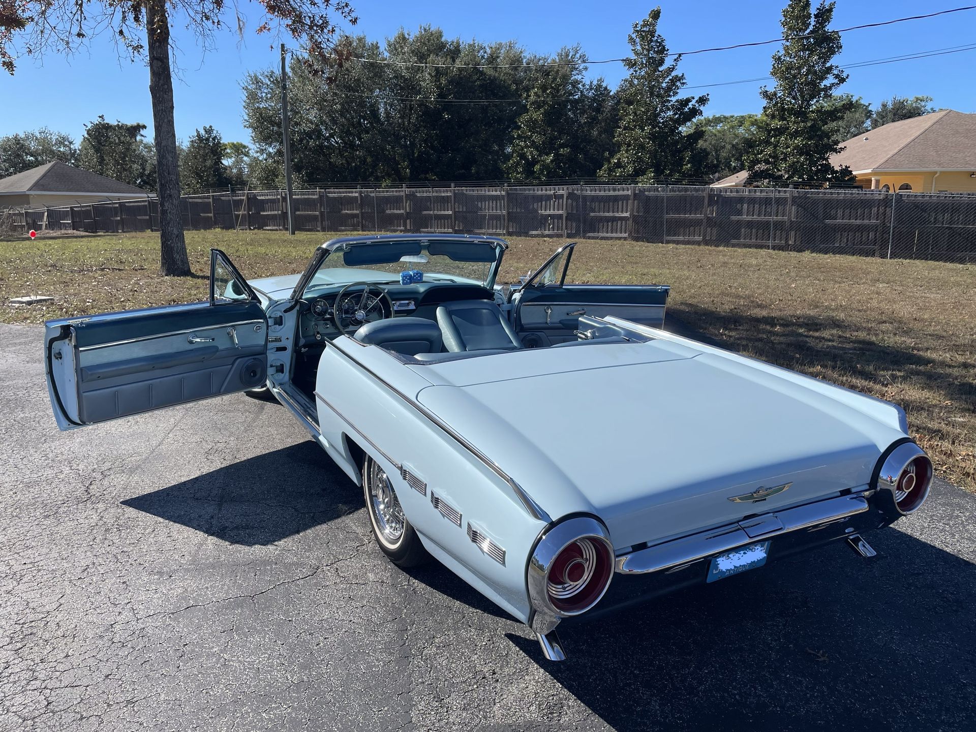 A light blue vintage Ford Thunderbird convertible with both doors open, parked on an asphalt lot.