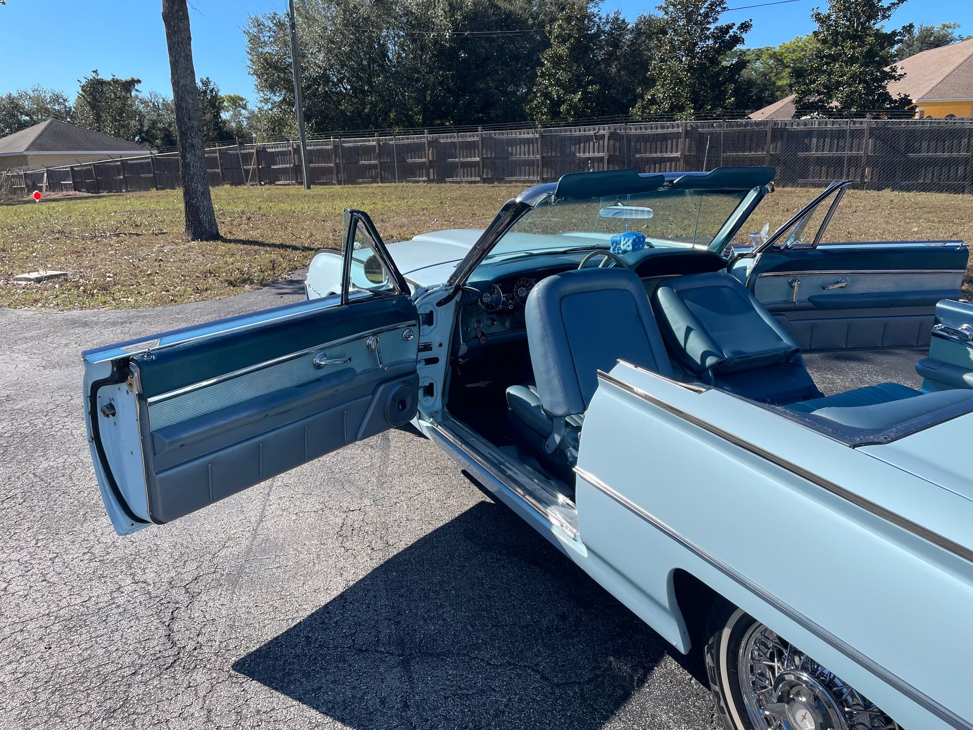 A pale blue vintage convertible with its doors open, parked on a gravel surface outdoors.