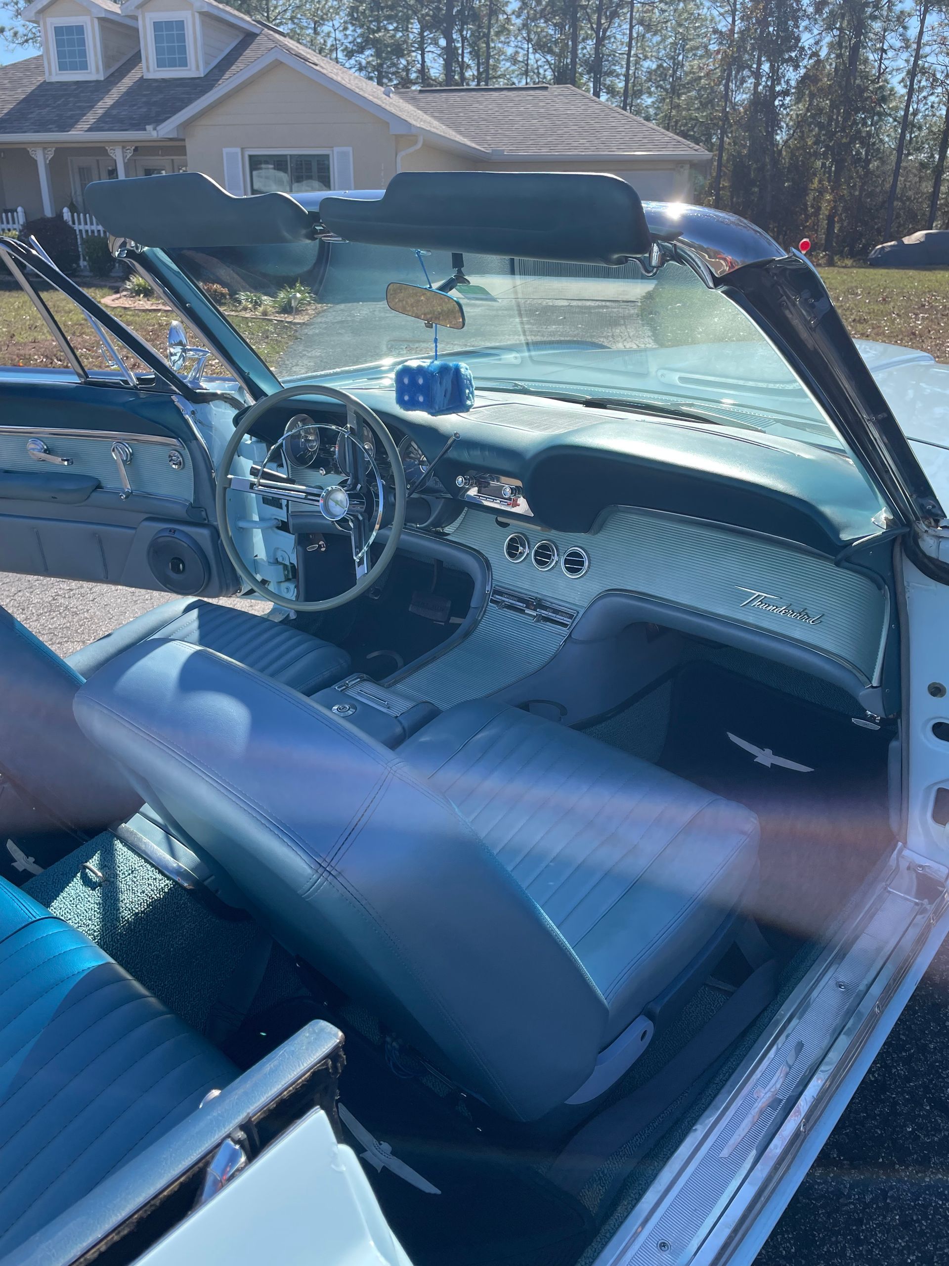 A bright blue interior of a classic convertible car parked in a driveway, featuring a chrome steering wheel and dashboard.
