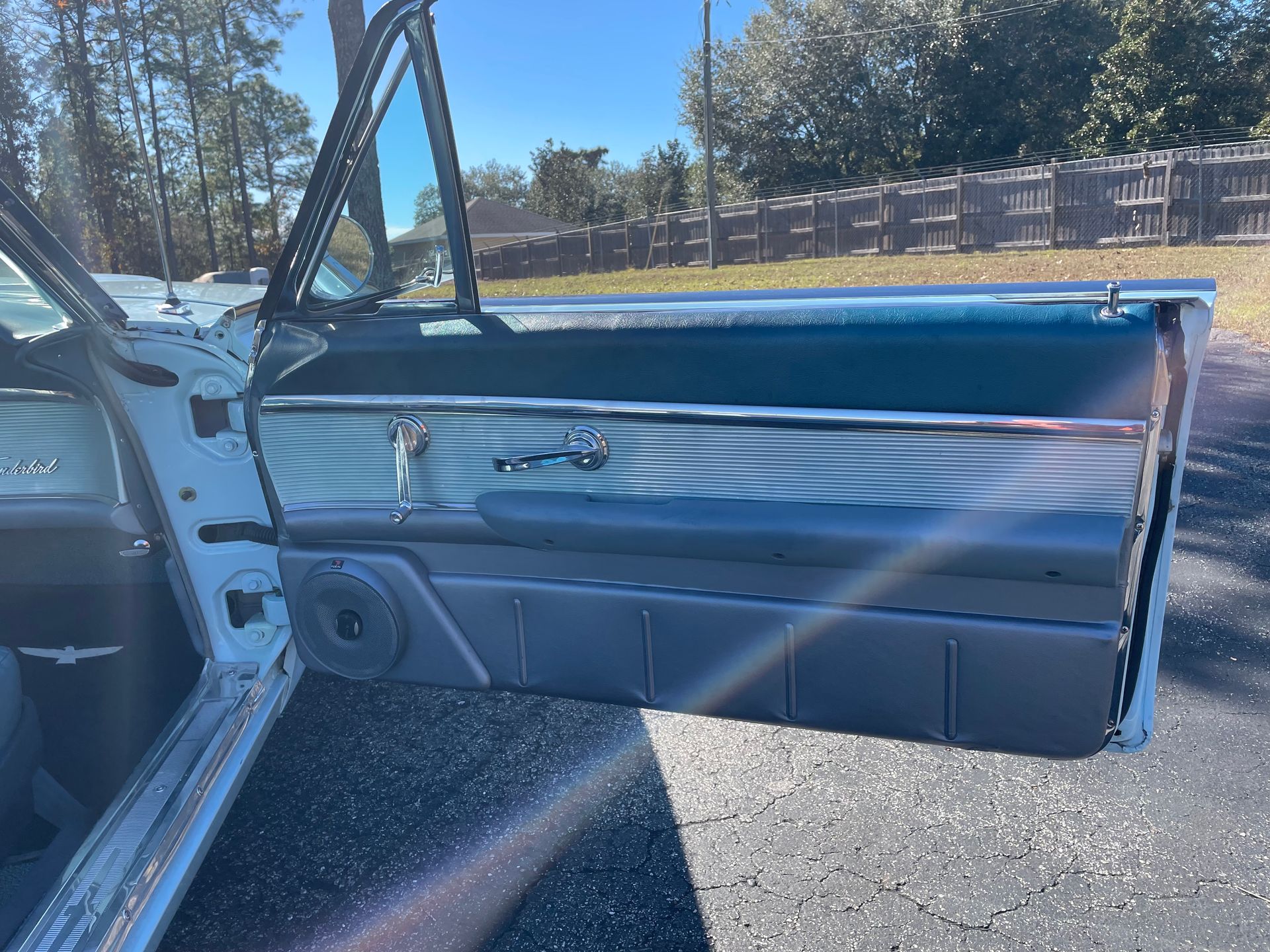 The open door of a vintage car, showing a blue interior panel, chrome trim, and an aftermarket speaker.