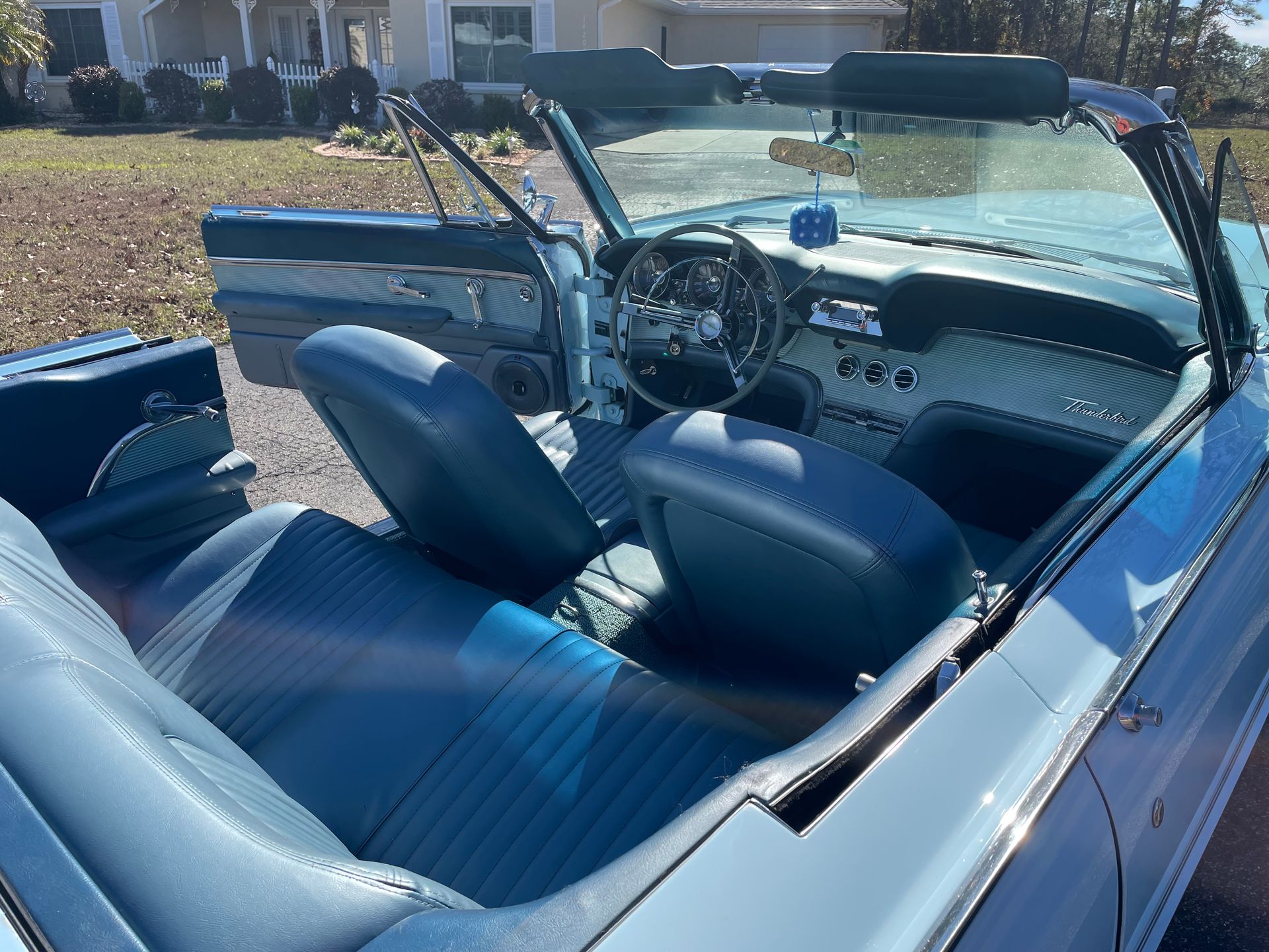 Interior of a light blue classic convertible with blue vinyl seats, a steering wheel, and a blue dice on the dashboard.