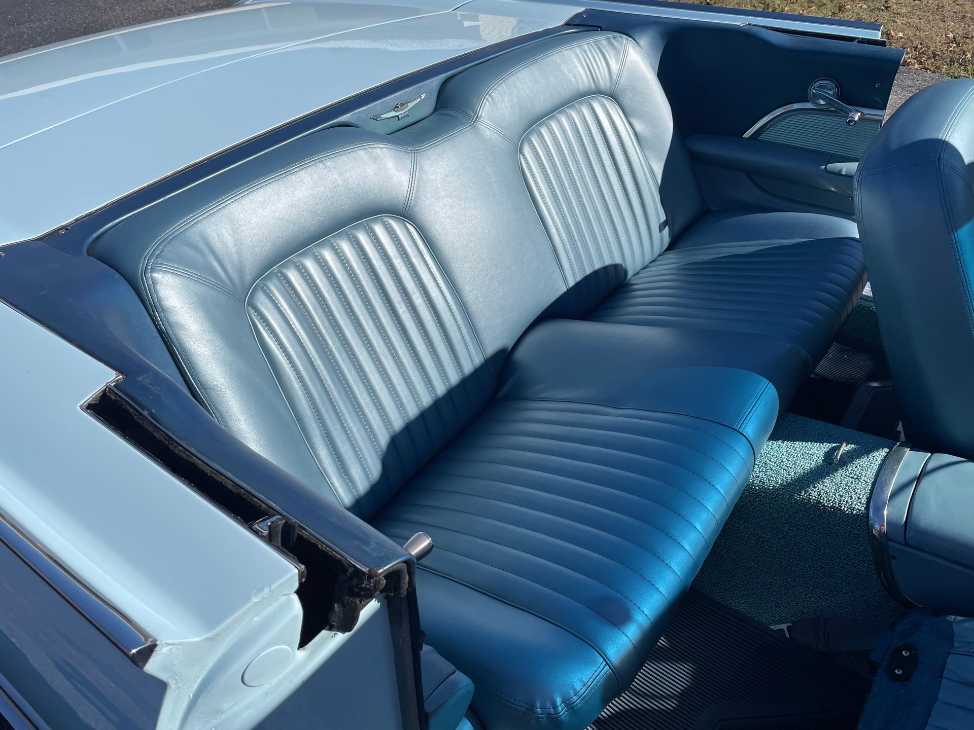 A close-up view of a classic convertible's rear bench seat upholstered in blue pleated vinyl.