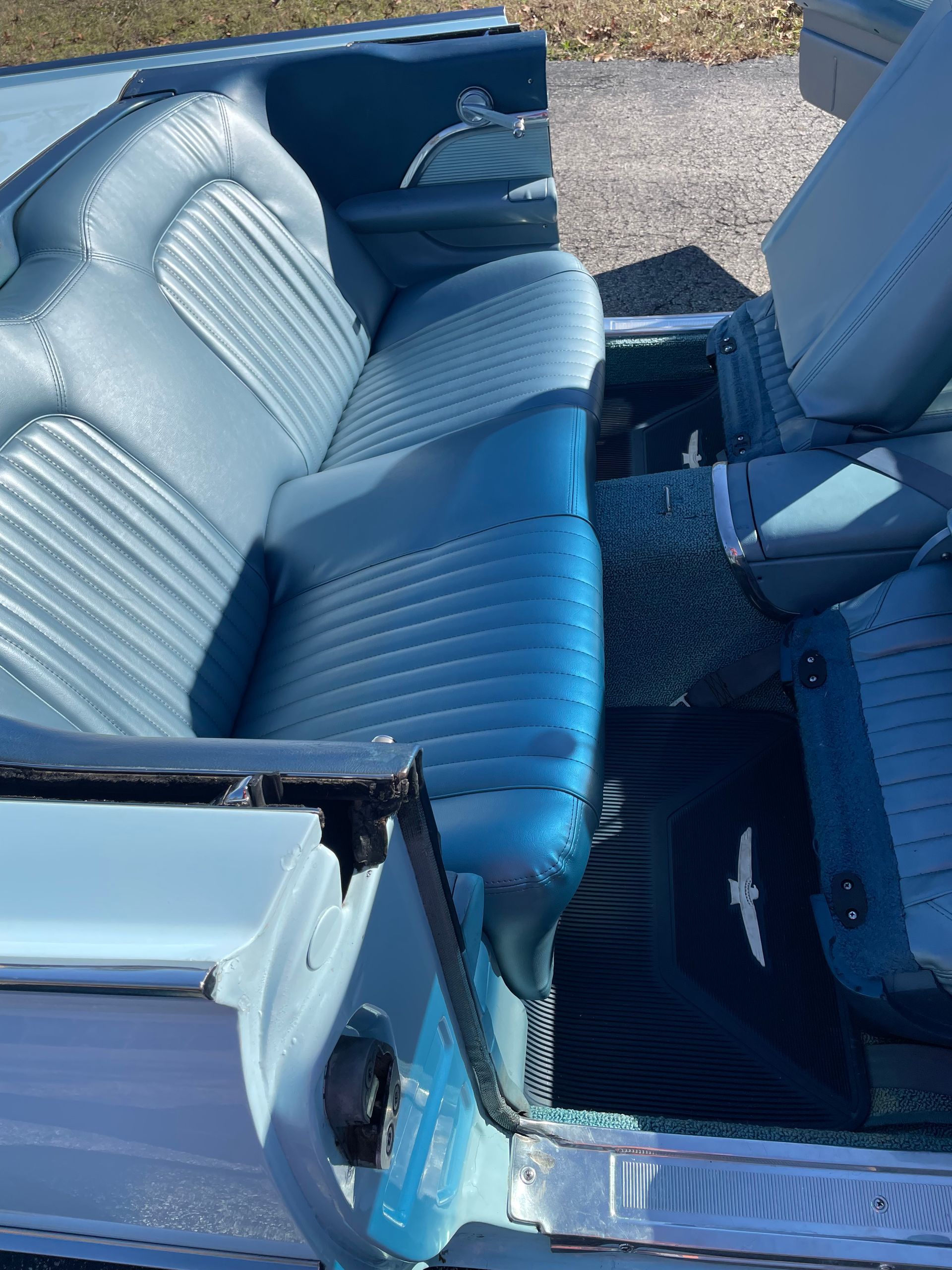 An interior view of a vintage convertible featuring blue textured leather bench seating and matching floor mats.