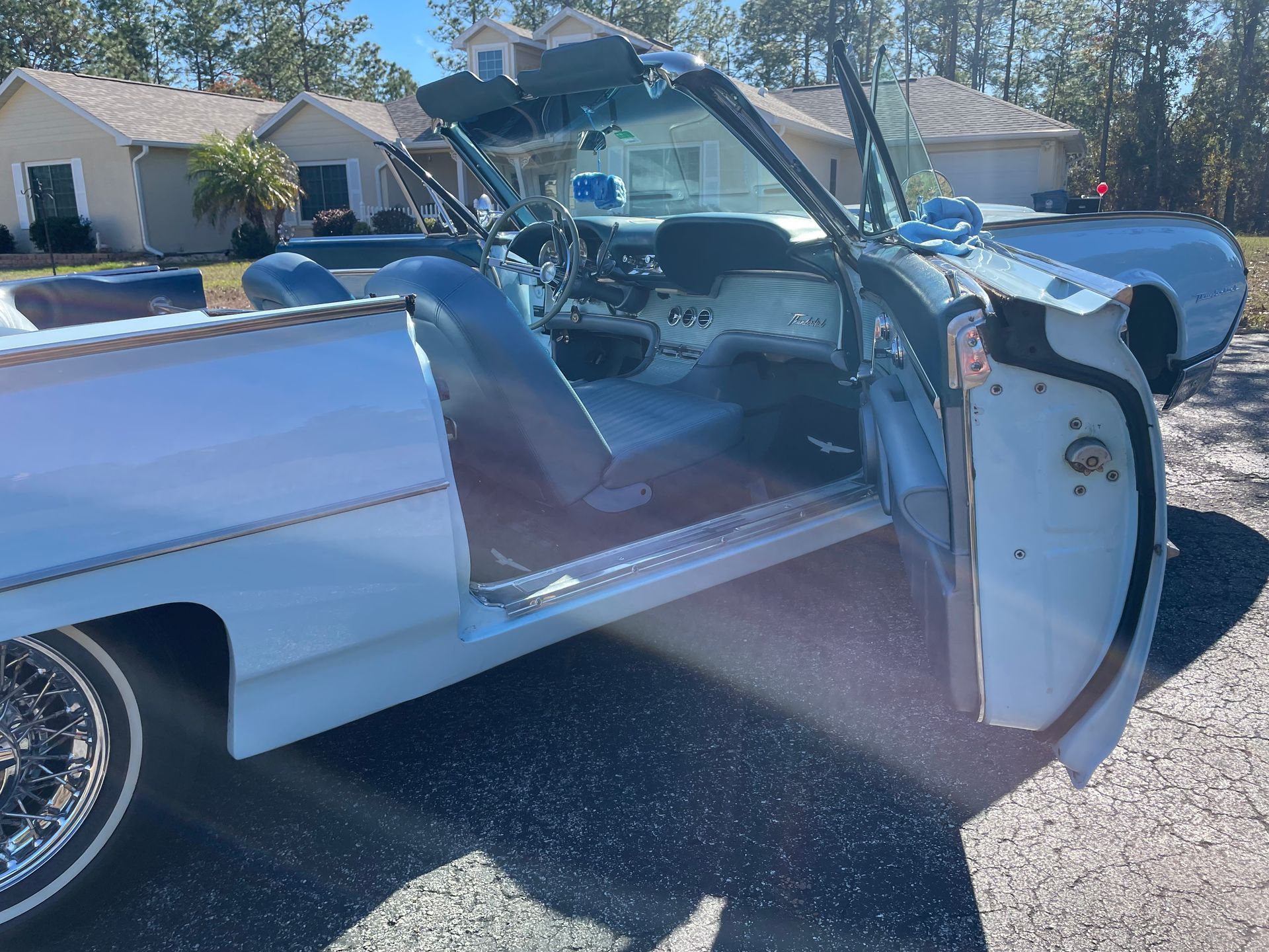 Light blue convertible car with doors open, parked on a driveway in front of a suburban house.