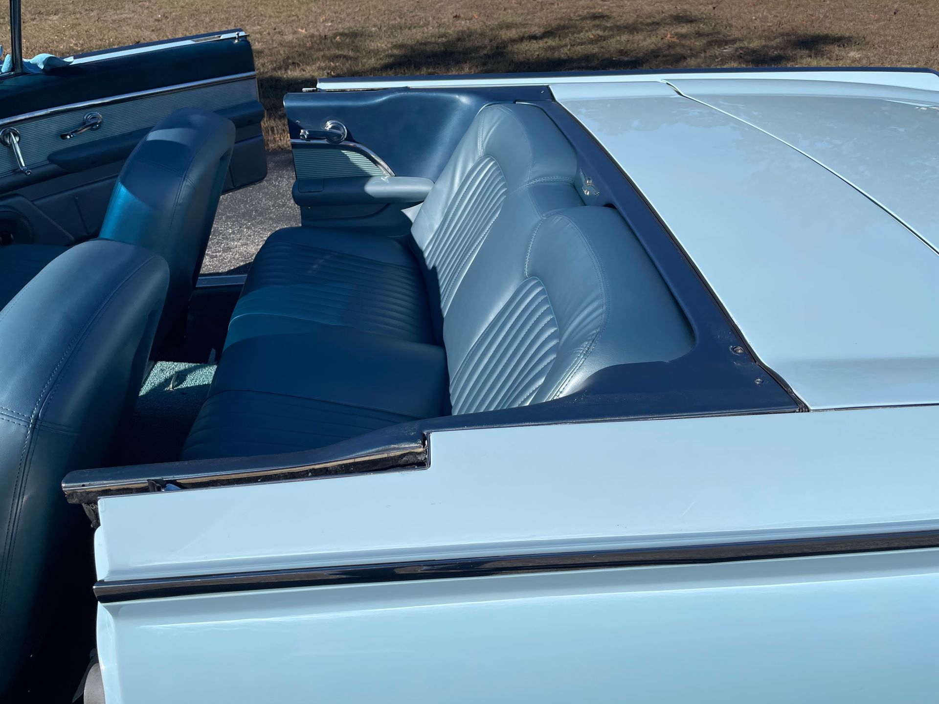 The interior of a convertible car, showing blue leather seats and a light-colored exterior body, parked outdoors.