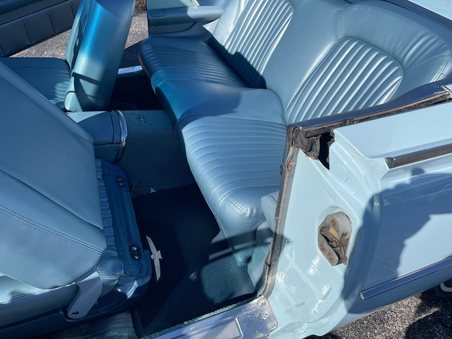 Interior of a classic convertible car featuring light blue pleated leather seats and dark blue carpet.