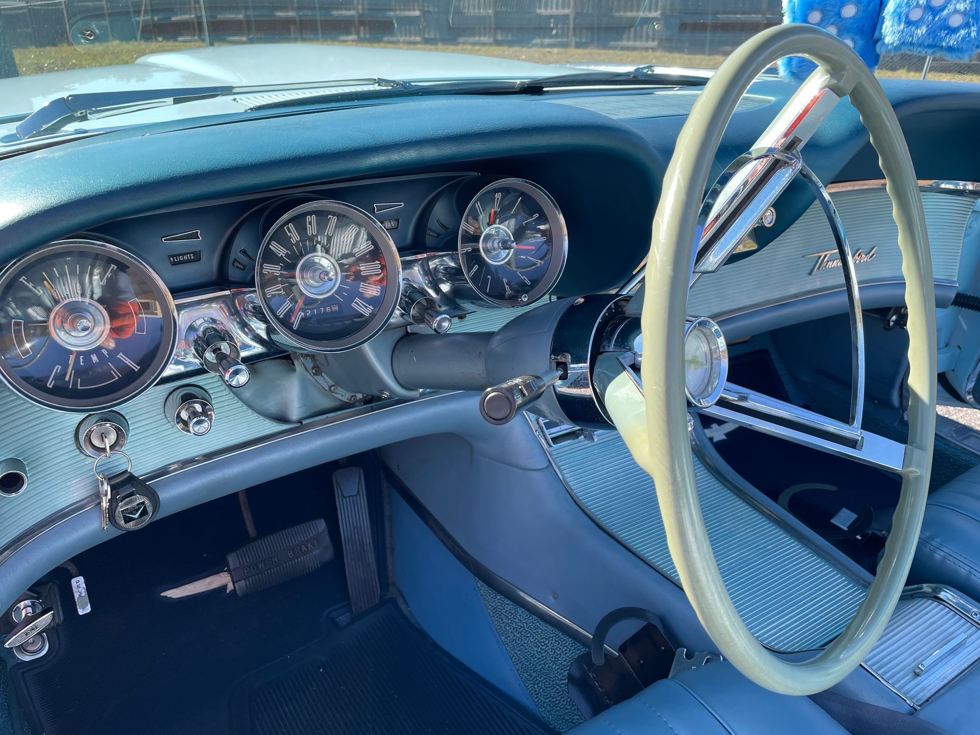 The interior of a vintage car featuring a large, light-colored steering wheel, blue dashboard, and circular analog gauges.