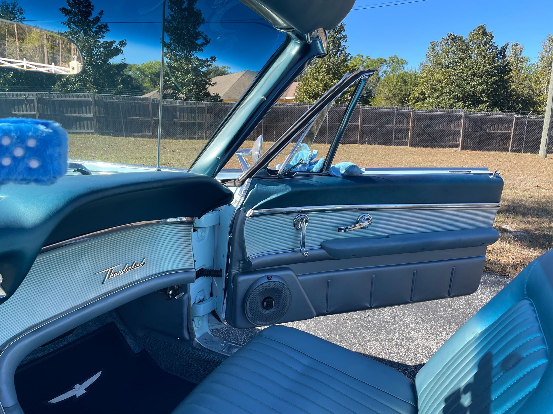 The interior of a classic teal Ford Thunderbird, showing the dashboard, driver-side door, and front seat.