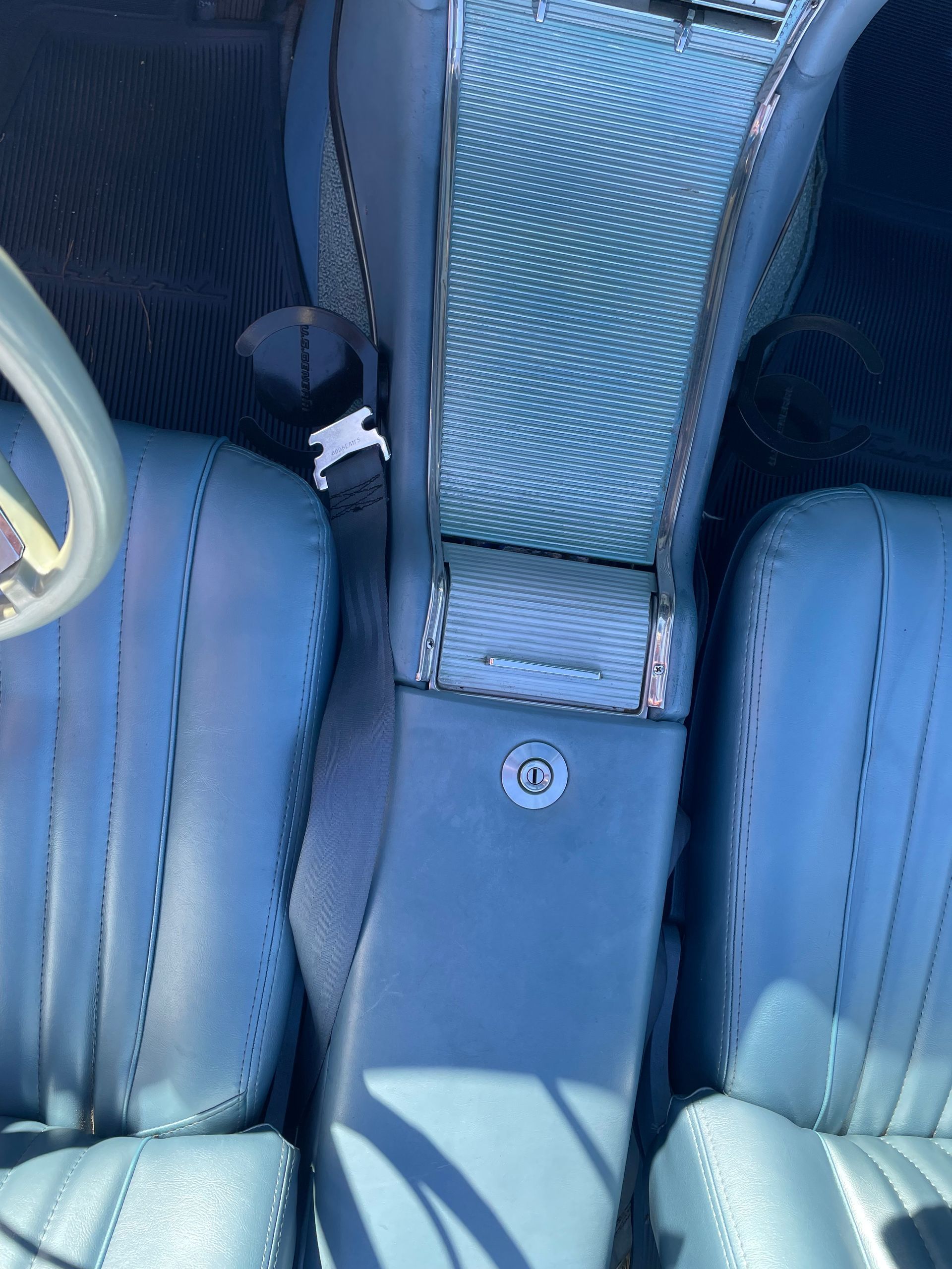 Blue car interior showing a textured center console, seatbelts, and stitched leather seats.
