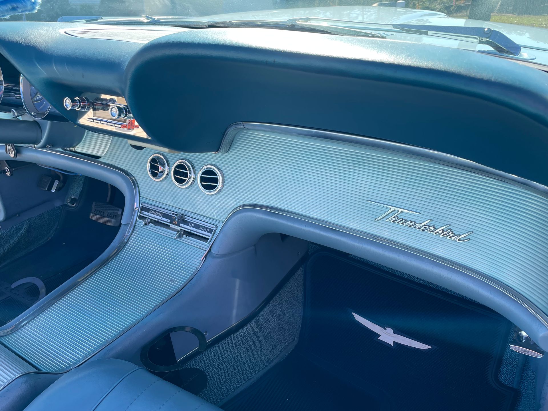 The interior dashboard and footwell of a vintage blue Ford Thunderbird with distinct engine-turned metal trim.