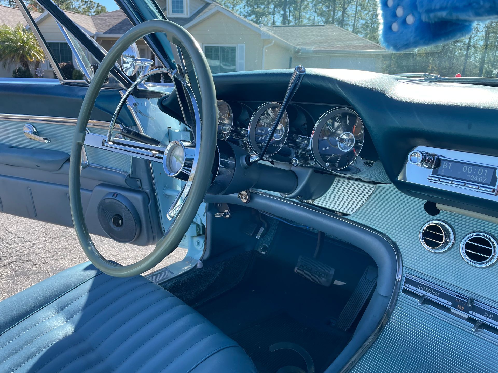 Interior view of a vintage car with blue leather seats, a light-colored steering wheel, and a classic metal dashboard.