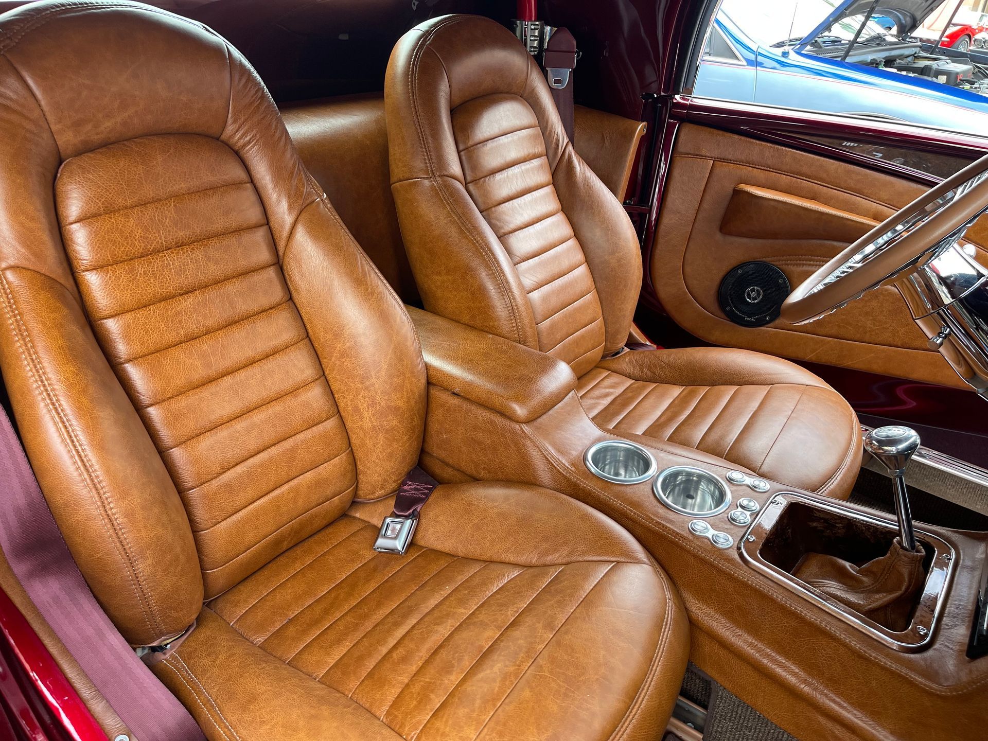 Interior view of a custom vehicle featuring tan textured leather bucket seats, matching console, and chrome cup holders.