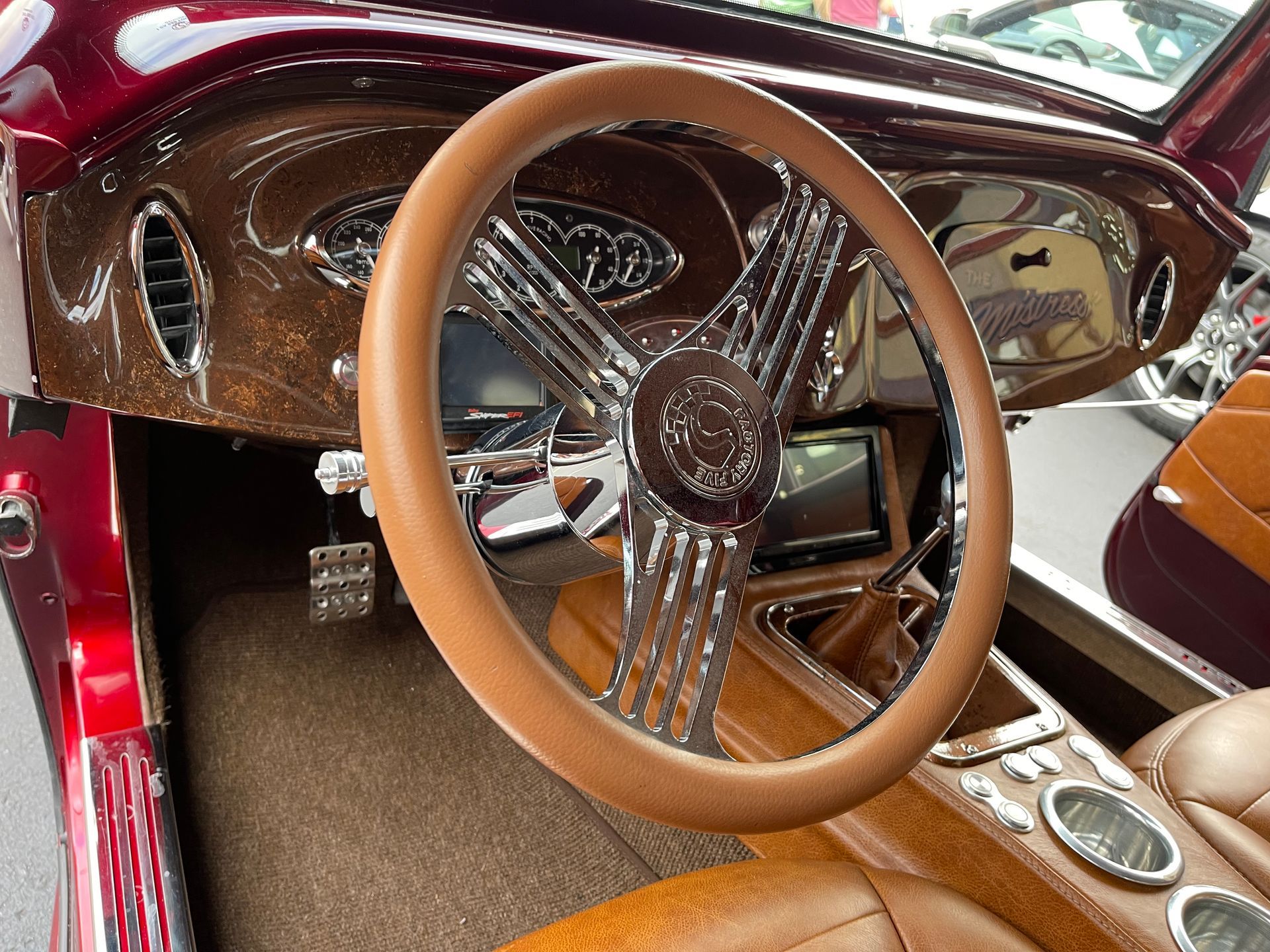 A custom car interior featuring a tan leather steering wheel, brown wood grain dashboard, and tan upholstery.