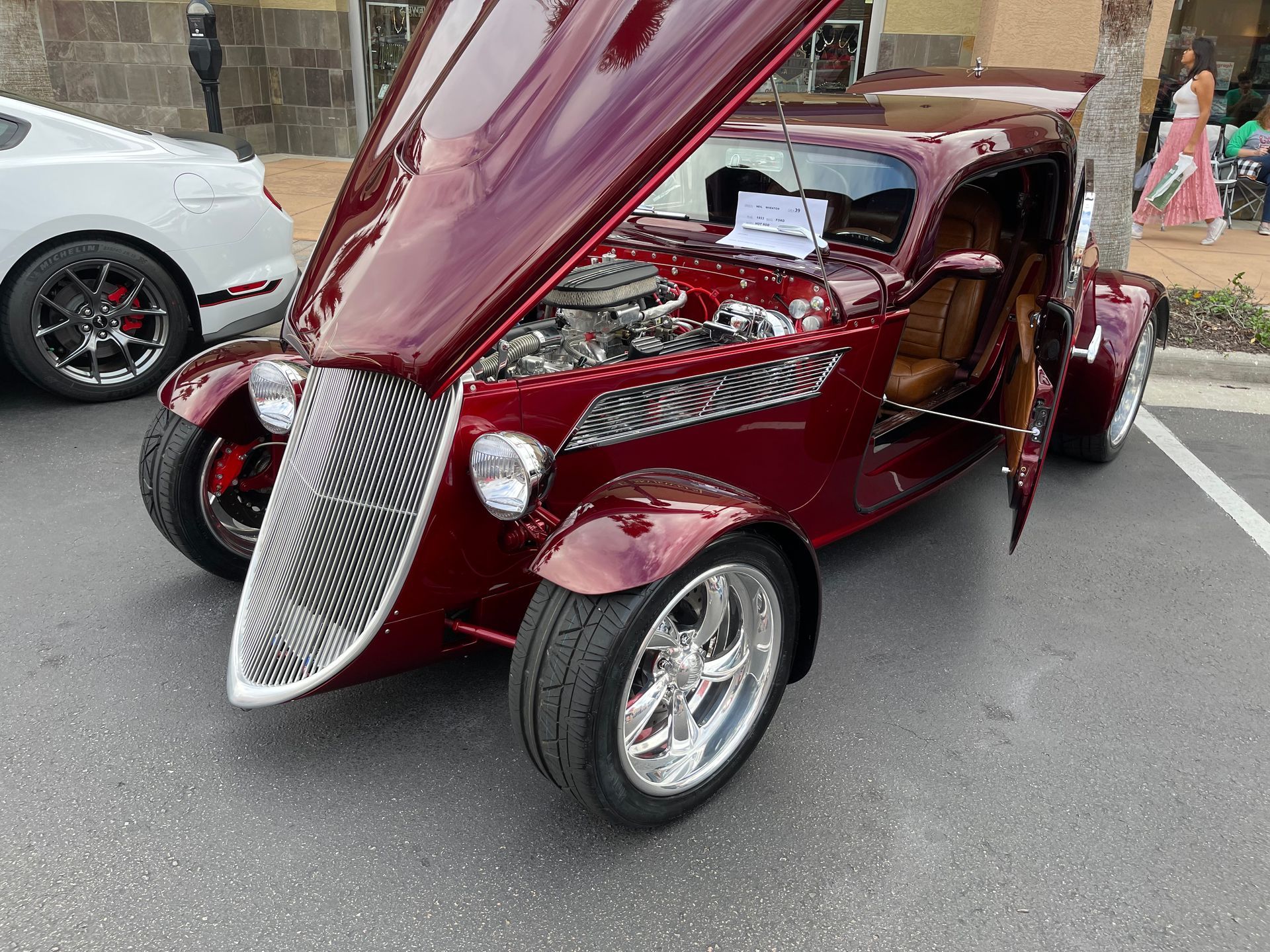 A polished, metallic-maroon custom hot rod with its hood and doors open, parked in an asphalt lot.