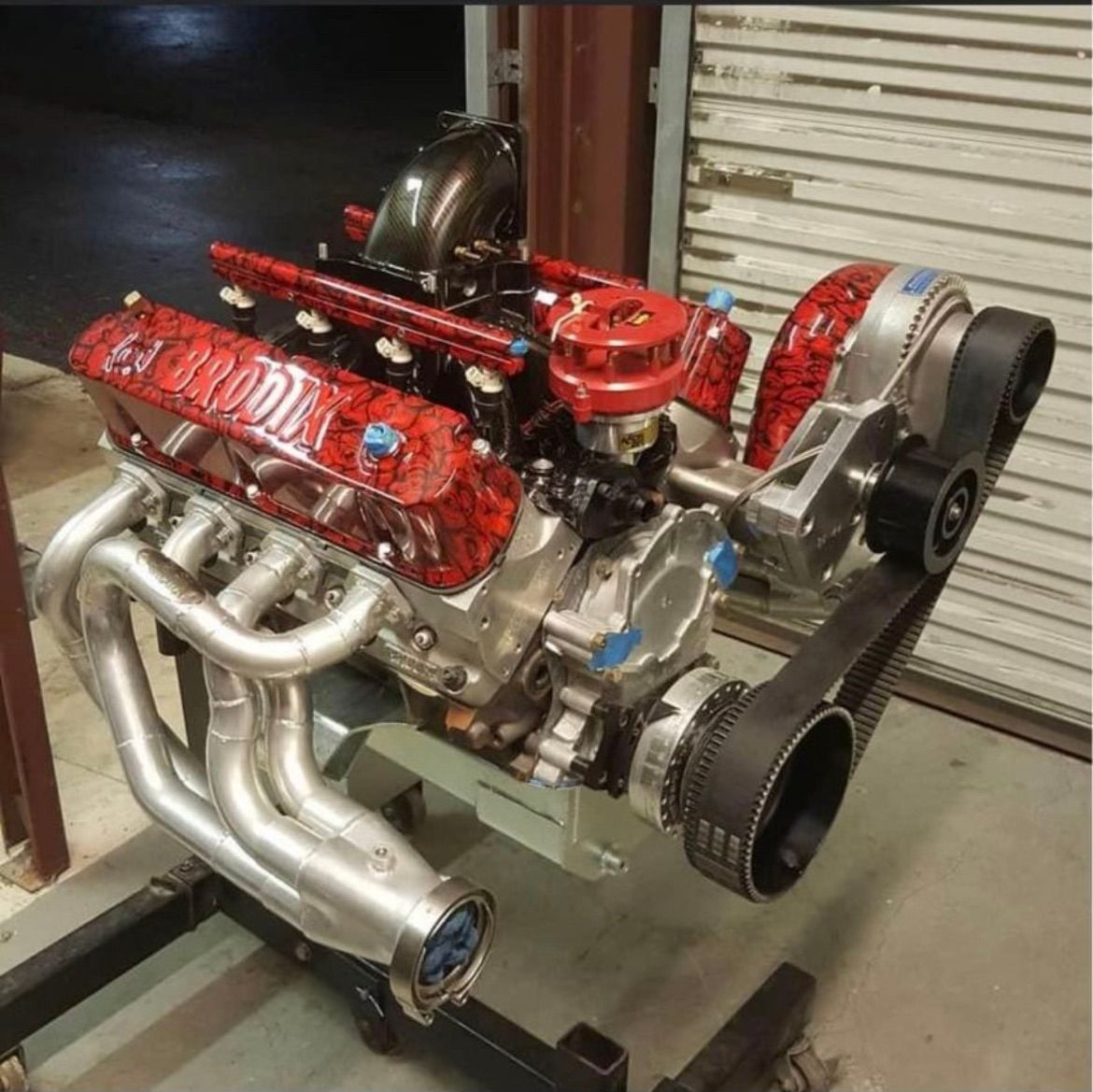 A high-performance V8 engine with red marbled valve covers and a front-mounted supercharger on an engine stand.
