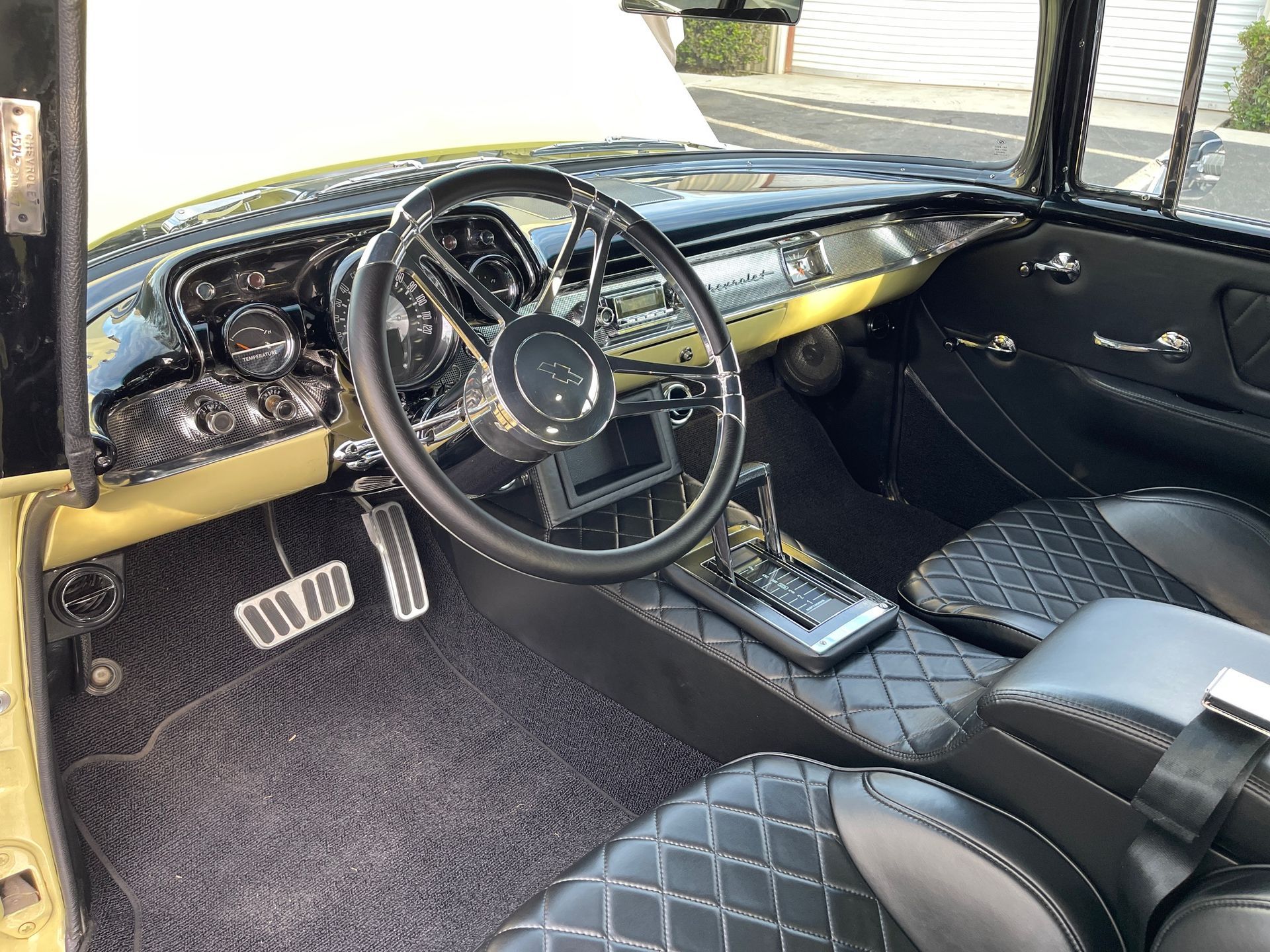 The interior of a classic car featuring a black quilted leather dashboard, seats, and a custom steering wheel.