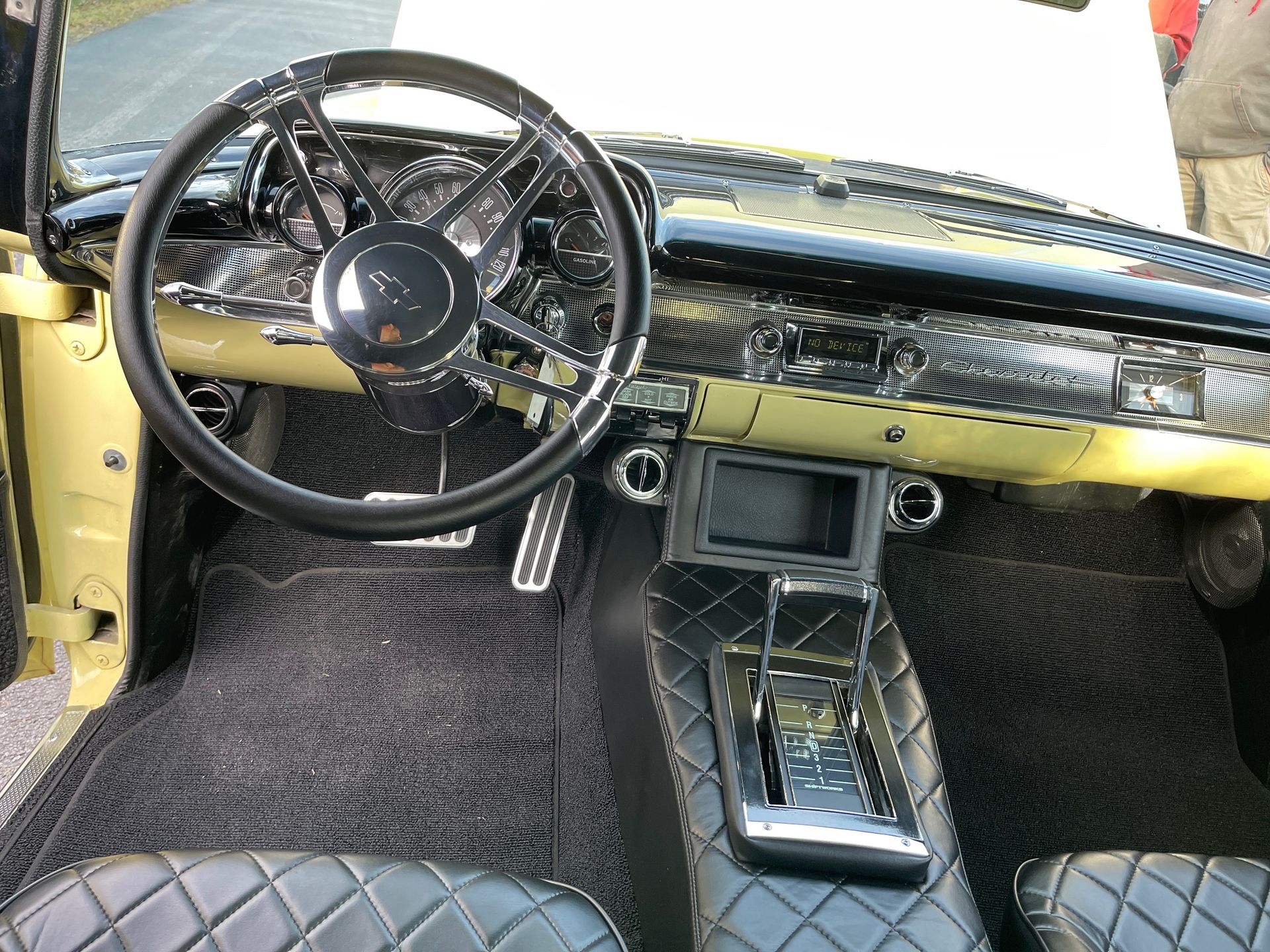 Interior of a classic car with a black leather diamond-stitched console and seats, a vintage steering wheel, and gauges.