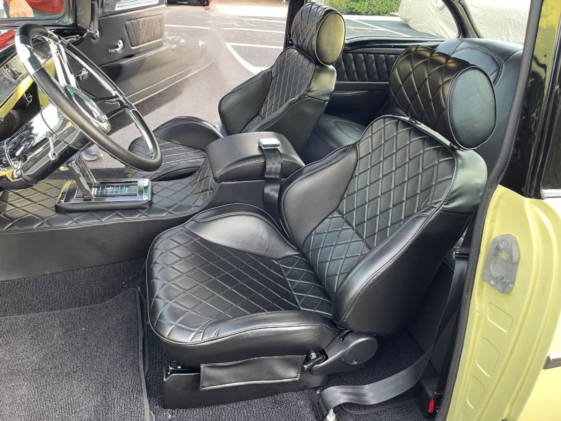 The interior of a classic car featuring custom black diamond-stitched leather bucket seats and a polished steering wheel.