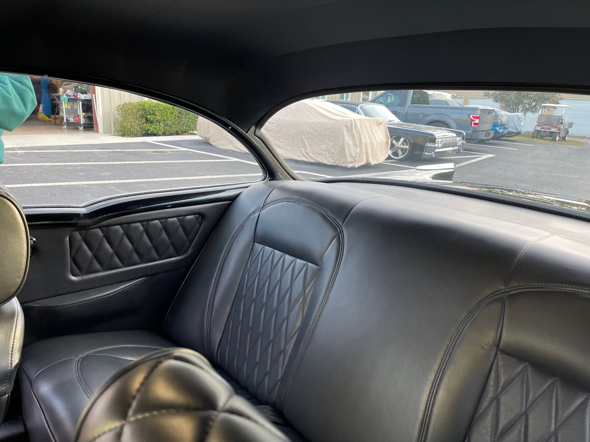 A car interior featuring black quilted leather seats and panels, viewed from the back seat looking out the rear window.