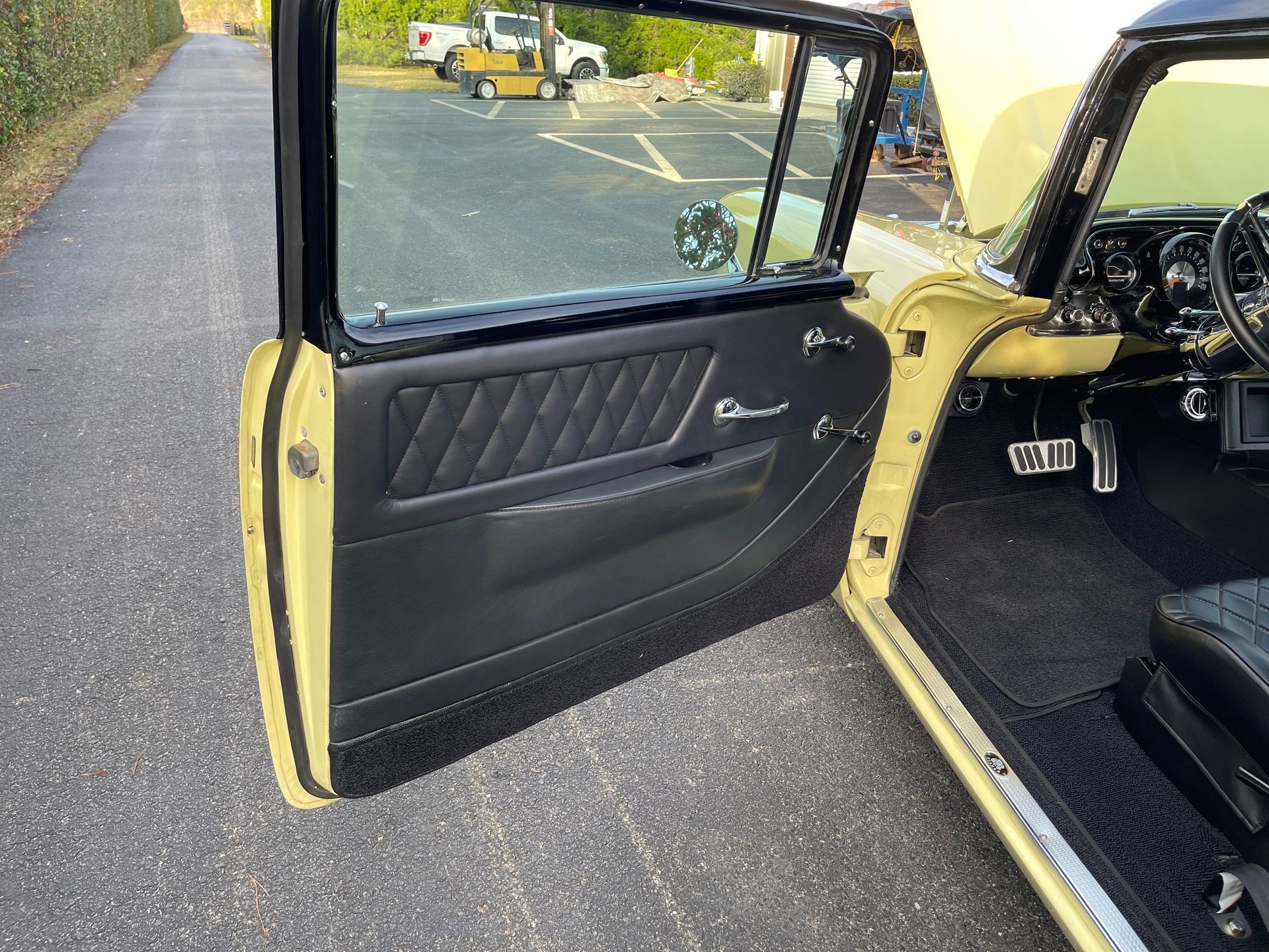 Open driver-side door of a vintage yellow car with black leather interior, parked on an asphalt lot.