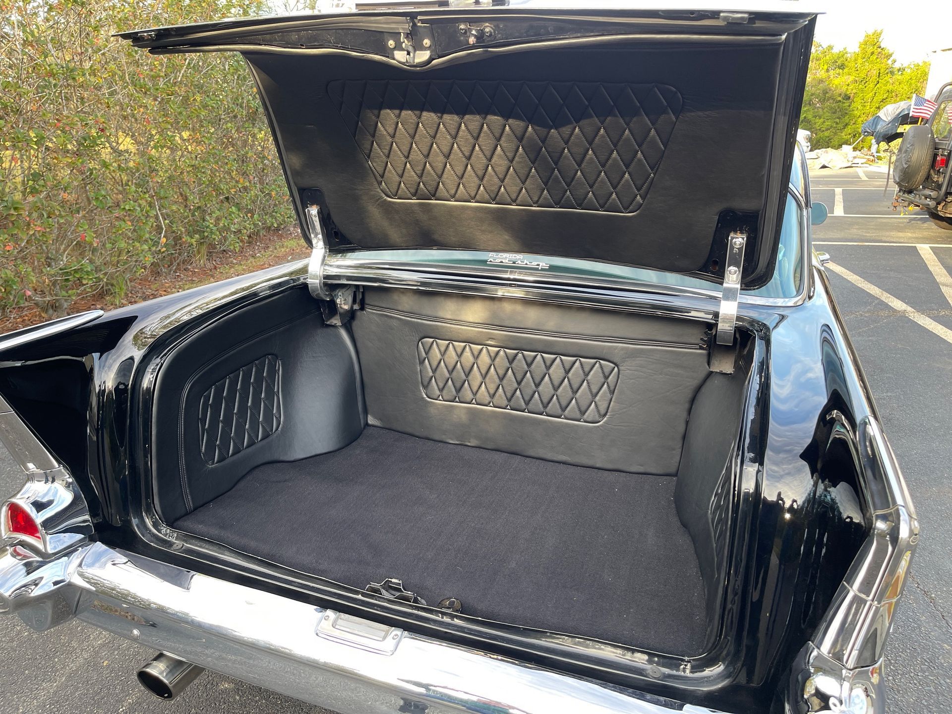 The open trunk of a black vintage car, featuring custom black diamond-stitched upholstery and a dark carpeted floor.
