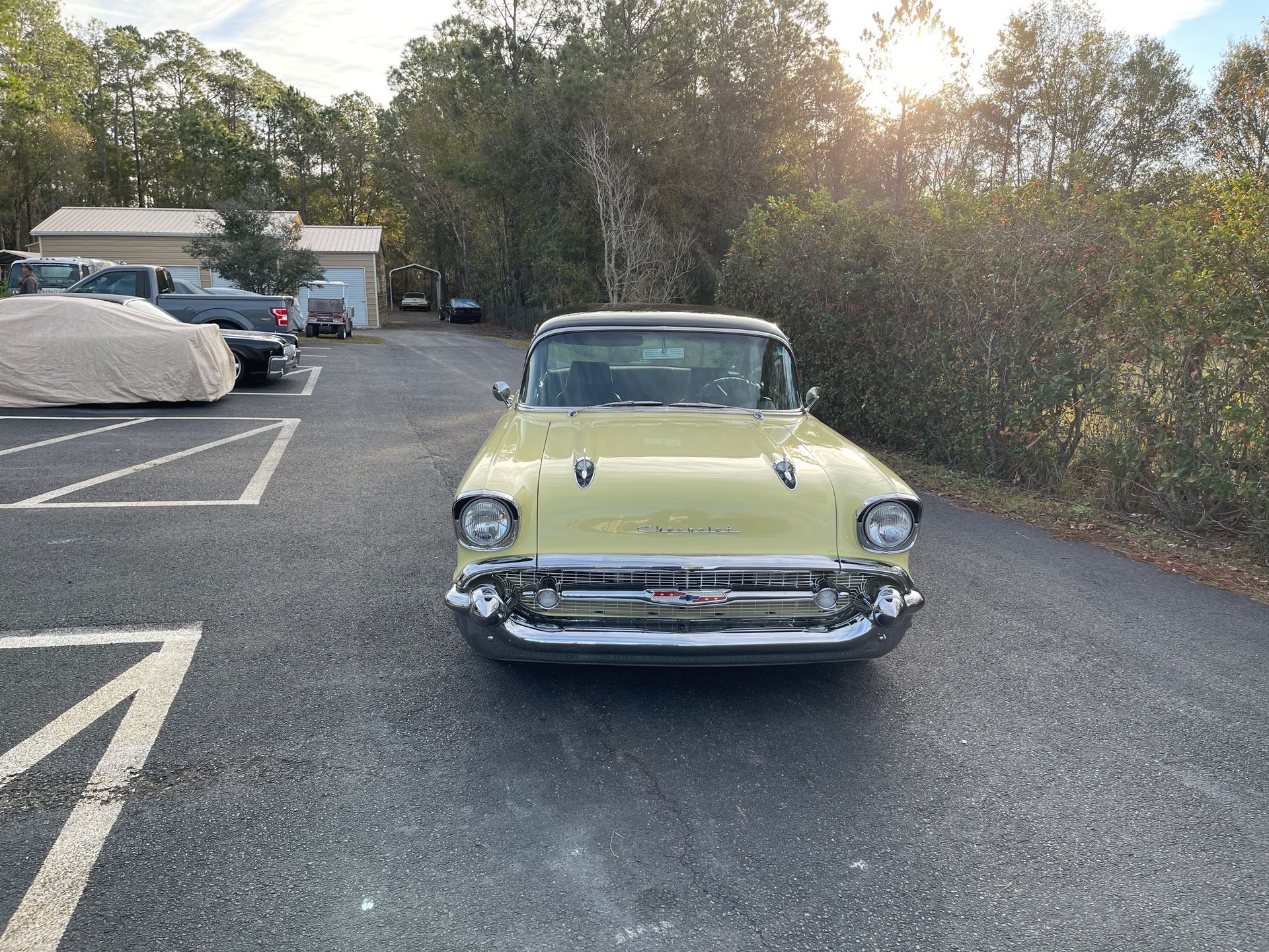 A vintage light yellow Chevrolet Bel Air parked in an outdoor gravel lot with trees in the background.