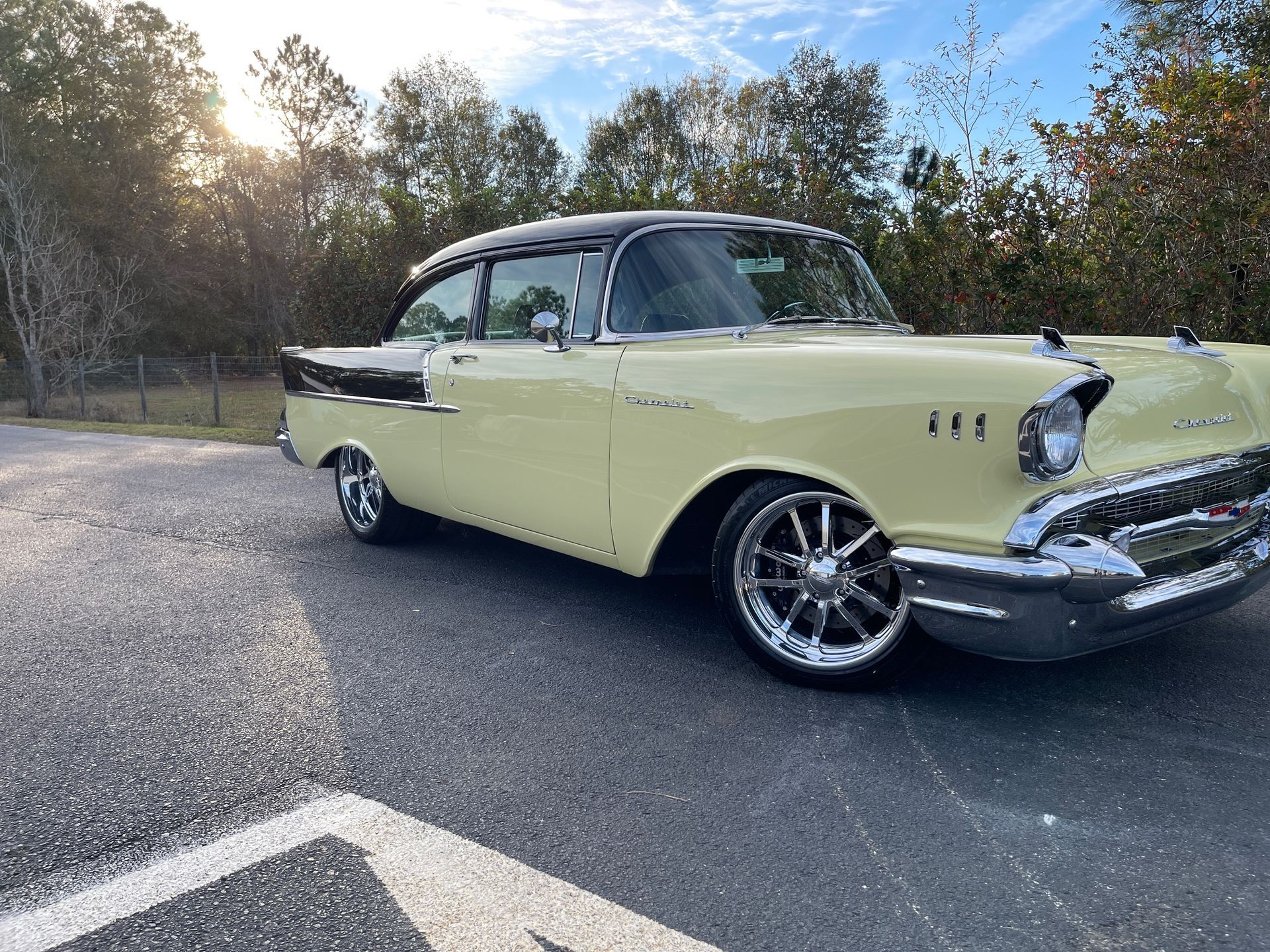 A pale yellow and black 1957 Chevrolet Bel Air parked on asphalt outdoors under a bright sky.