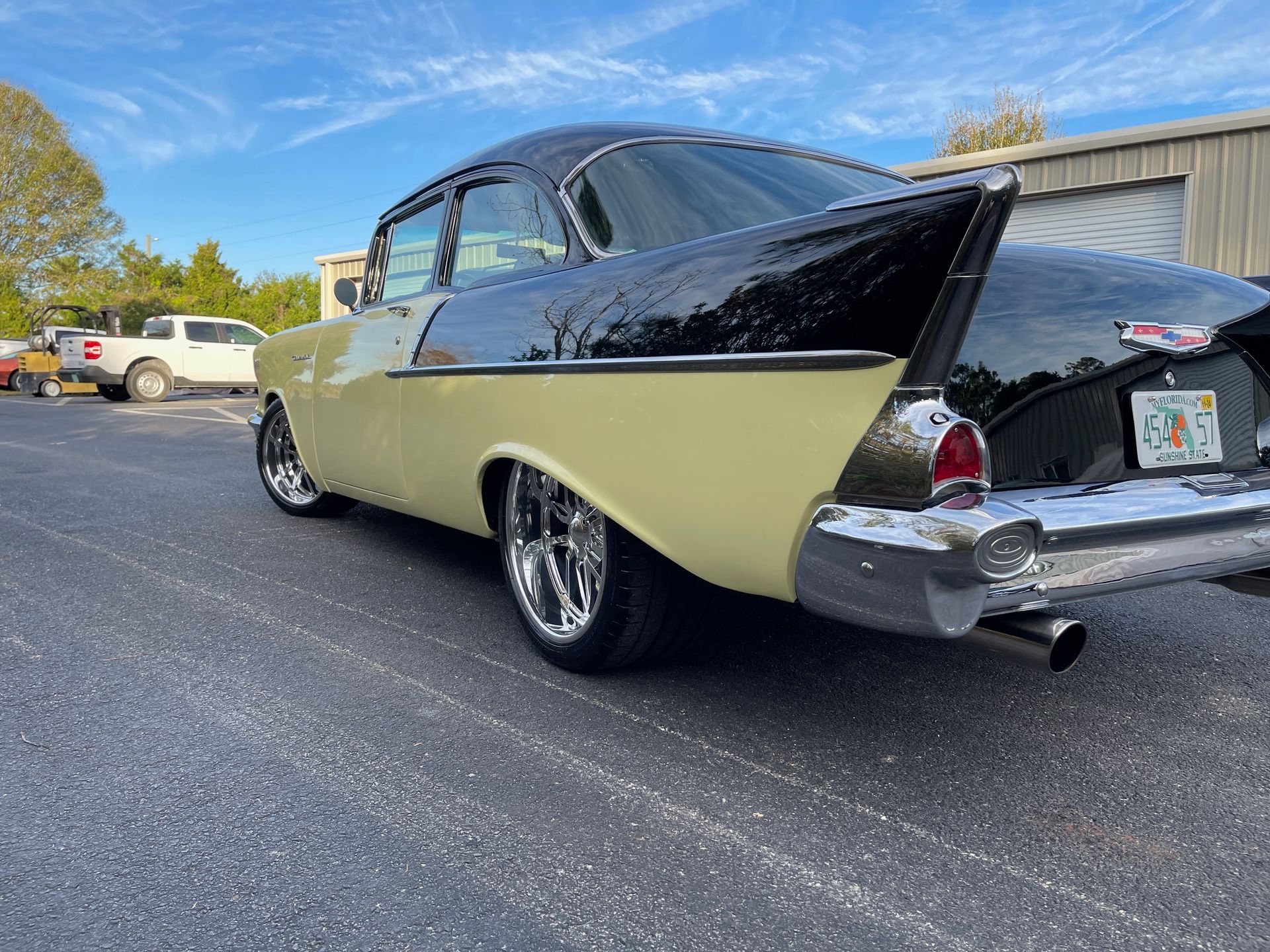 A two-tone yellow and black 1957 Chevrolet Bel Air parked in an asphalt lot on a sunny day.