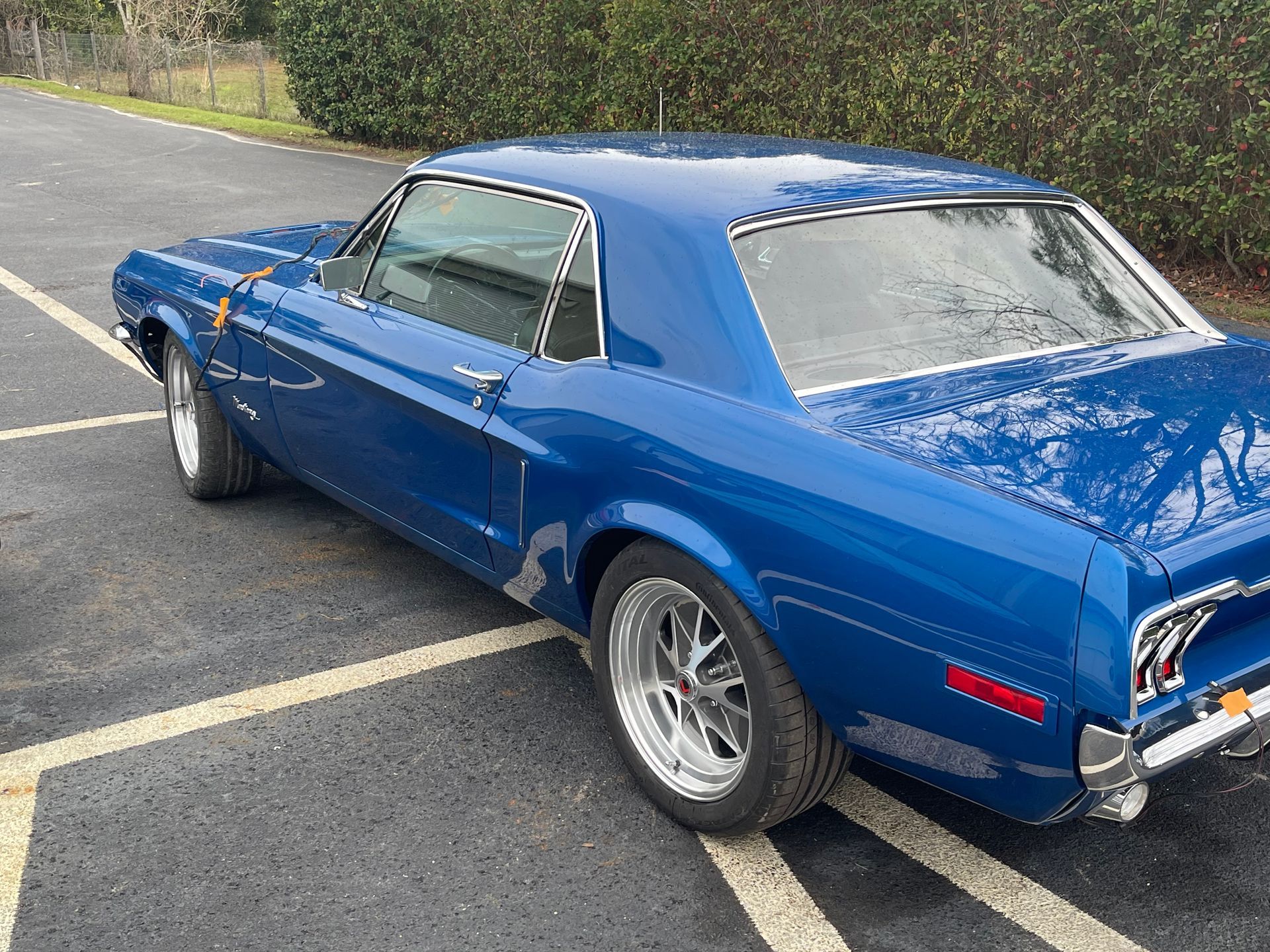 A blue vintage Ford Mustang coupe parked in an asphalt lot.