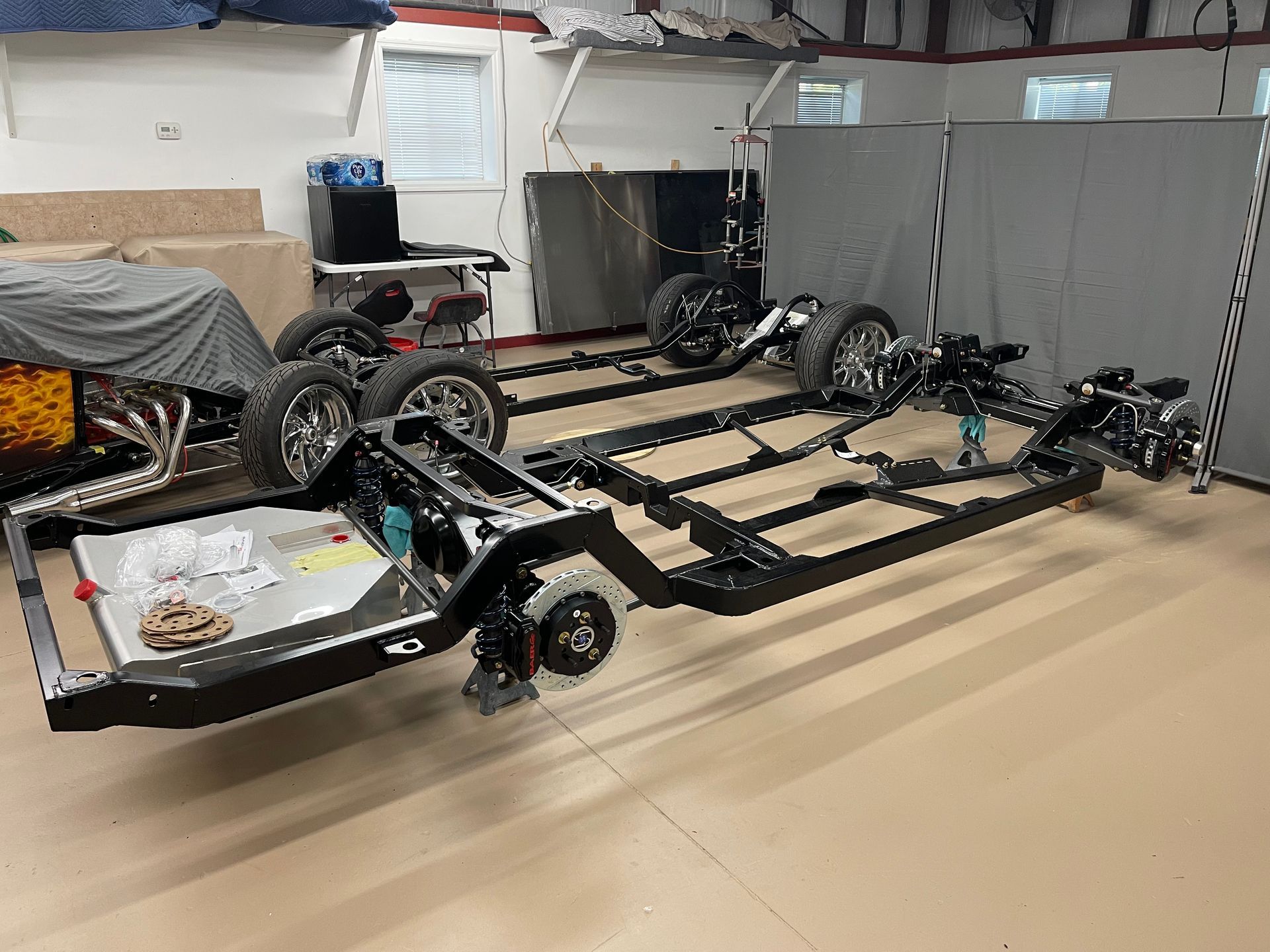 A black car chassis with tires and mechanical components sits on a workshop floor.