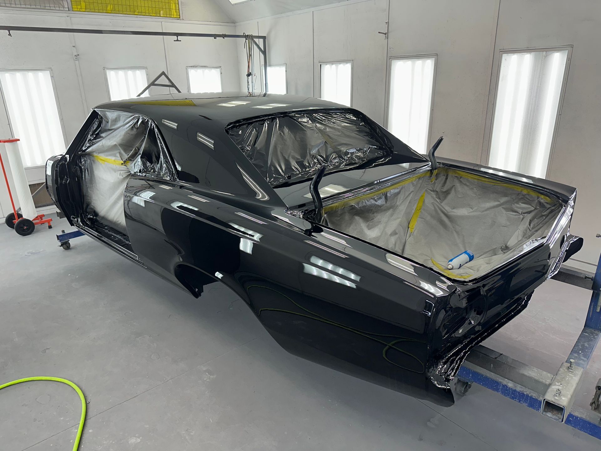A freshly painted, shiny black vintage muscle car body sits in a professional auto body paint booth.