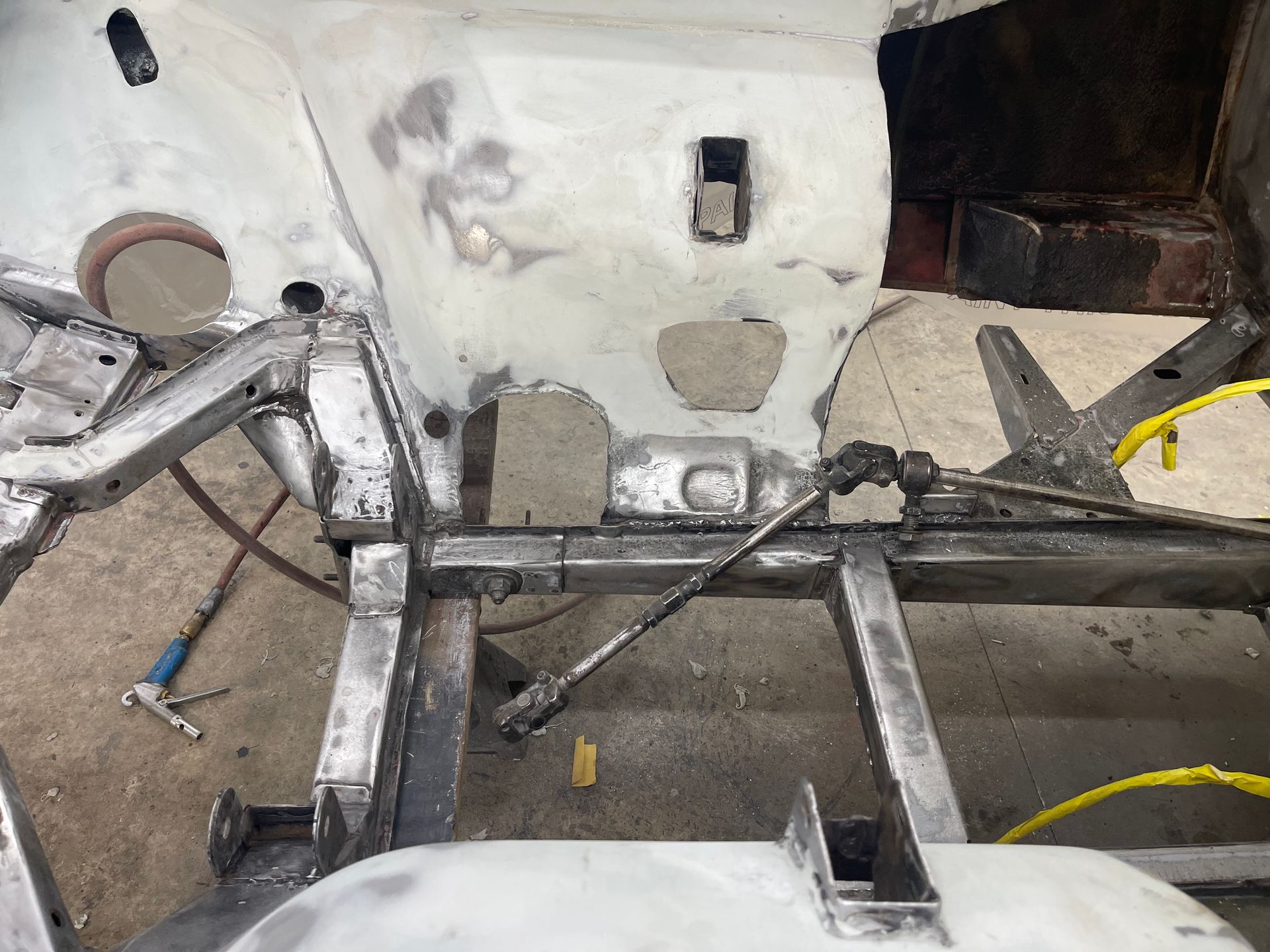 The metal chassis of a vehicle under restoration, featuring a steering column assembly connected to the frame.