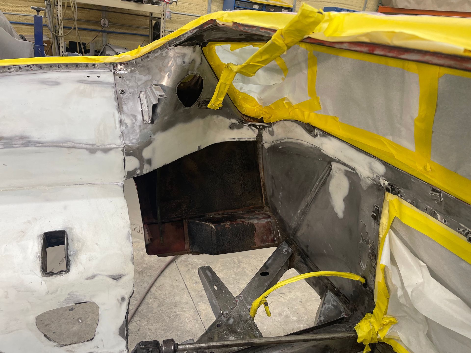 A partially stripped car interior undergoing restoration, with masked windshield areas and exposed metal panels.