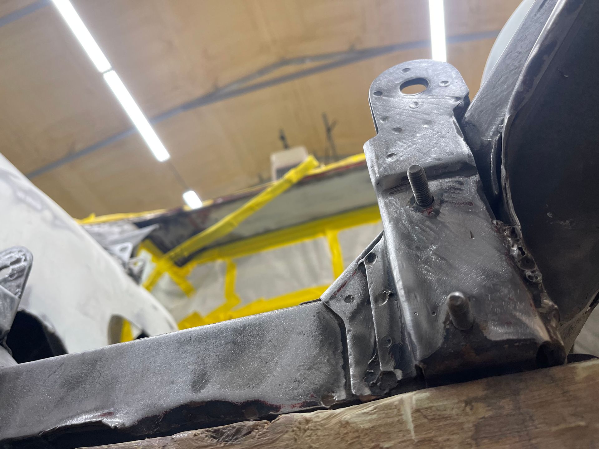 Close-up of a metal vehicle frame component being restored, featuring gray welded joints in an auto shop setting.