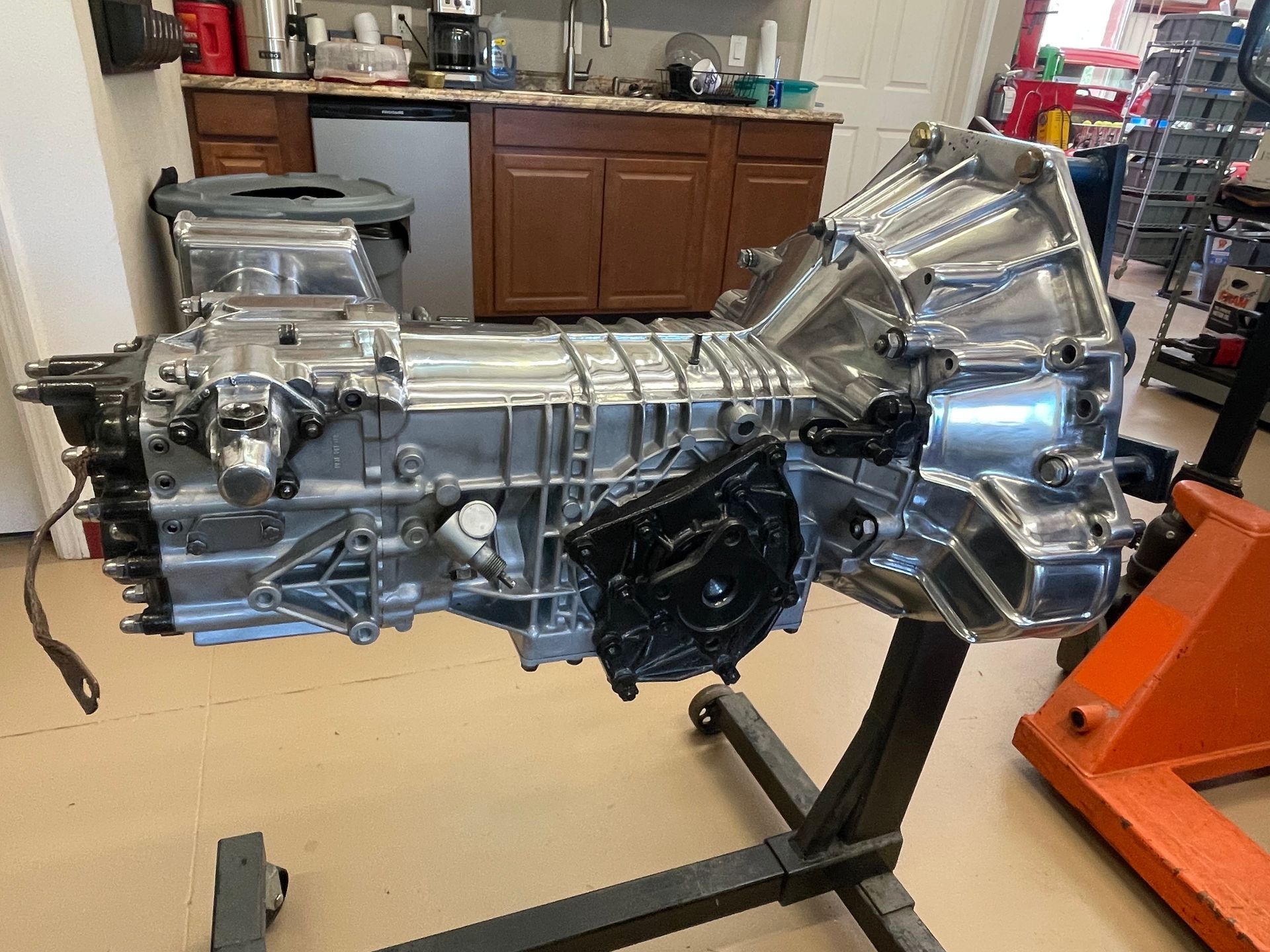 A clean, metal automotive transmission mounted on a black rolling stand in a workshop.