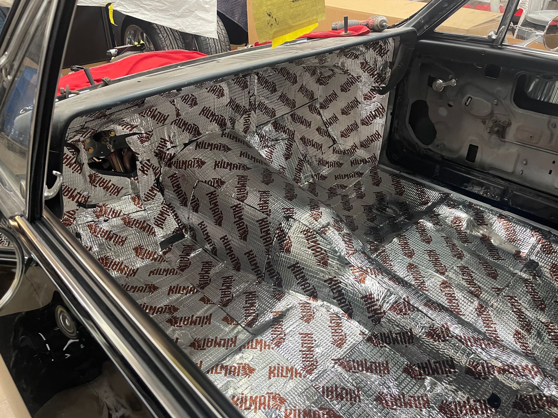 The interior floor and firewall of a car undergoing restoration, covered in silver-patterned sound-deadening material.
