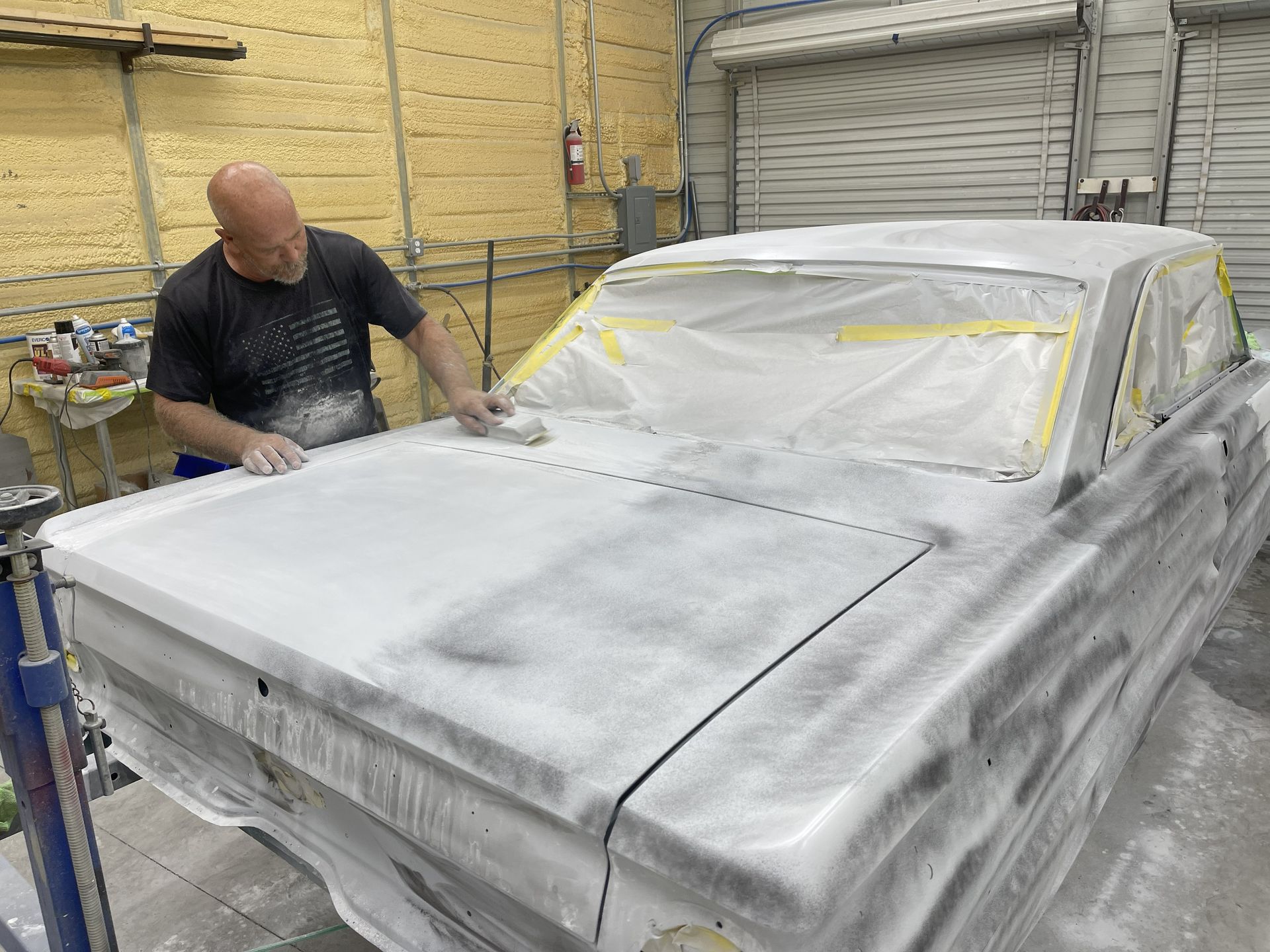 A person sands the white primer on the trunk of a car in a body shop.
