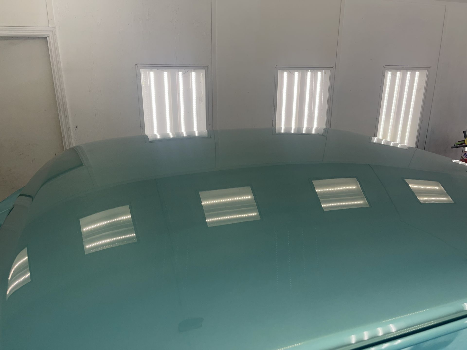 Glossy, teal-colored car roof reflecting rectangular workshop ceiling lights.