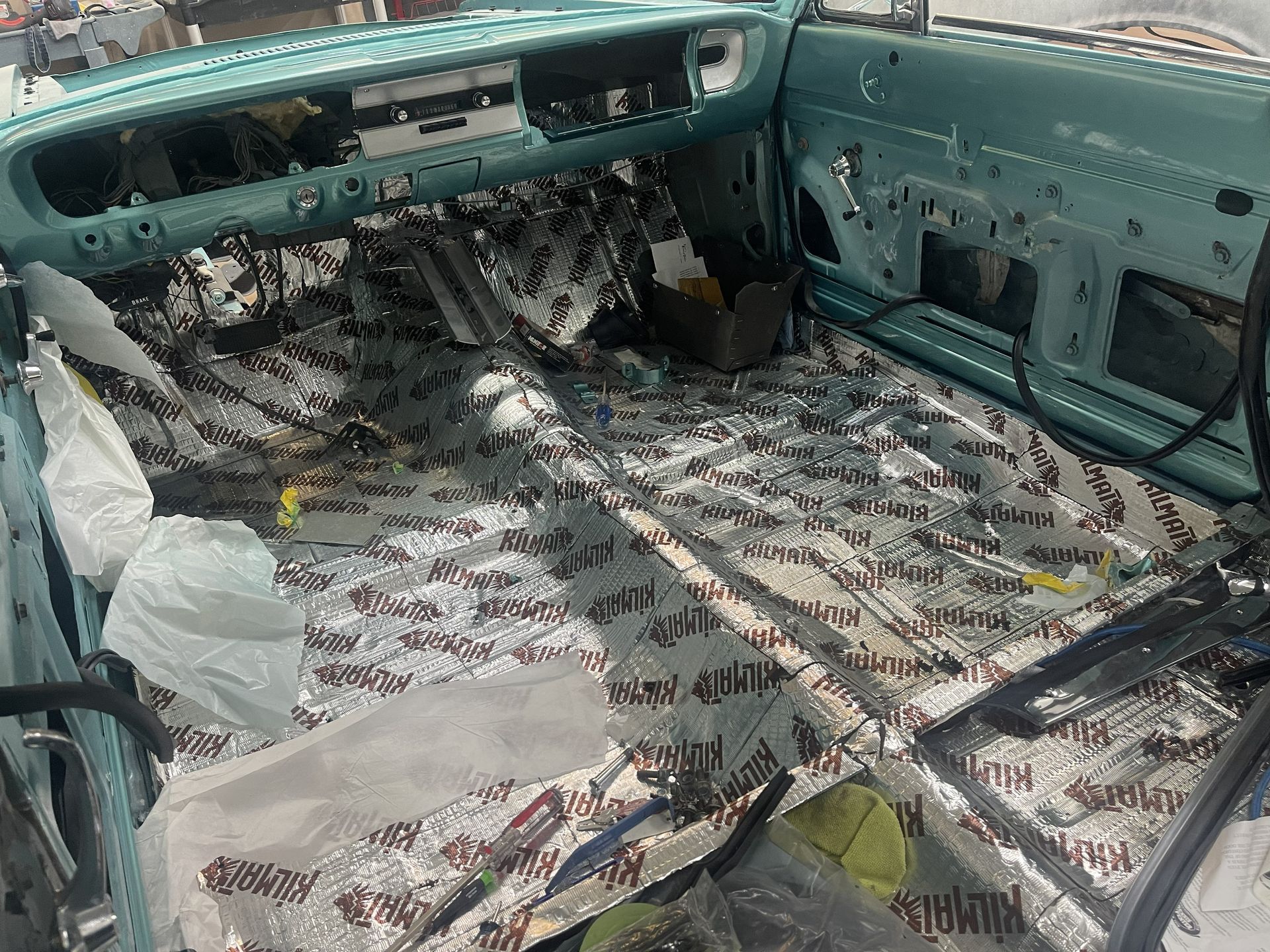 Interior of a classic car under renovation, featuring a light blue dashboard and sound-deadening material on the floor.